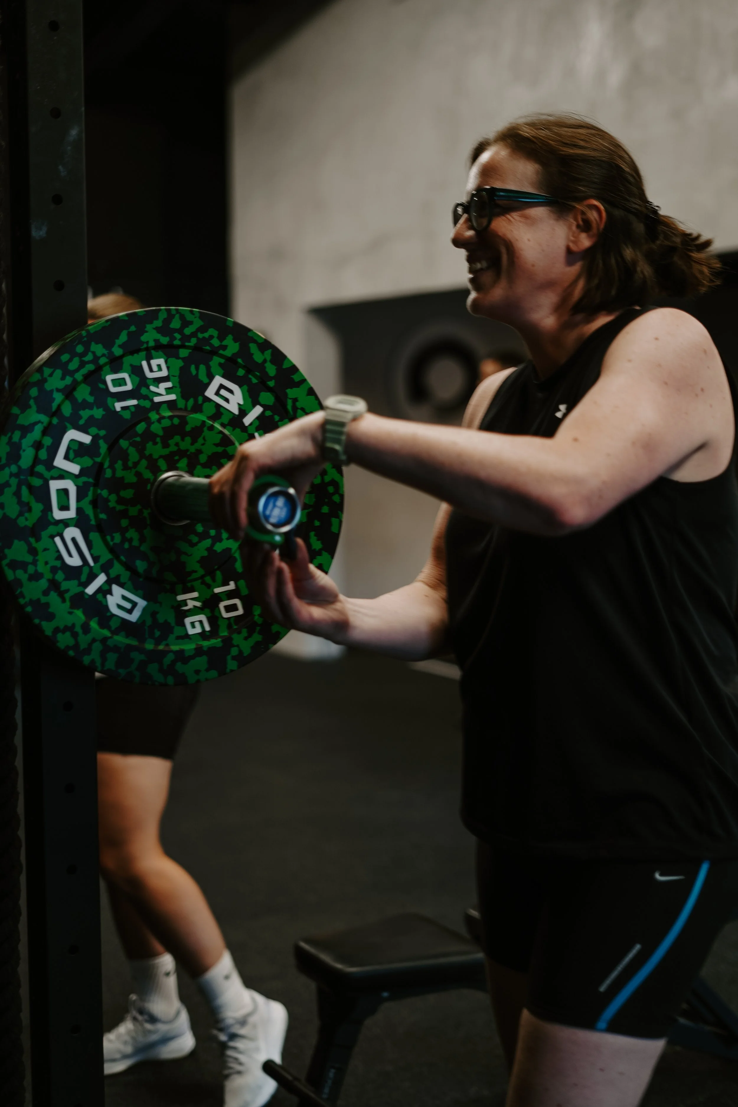 Woman smiling as she loads weight plates onto a barbell in a gym.