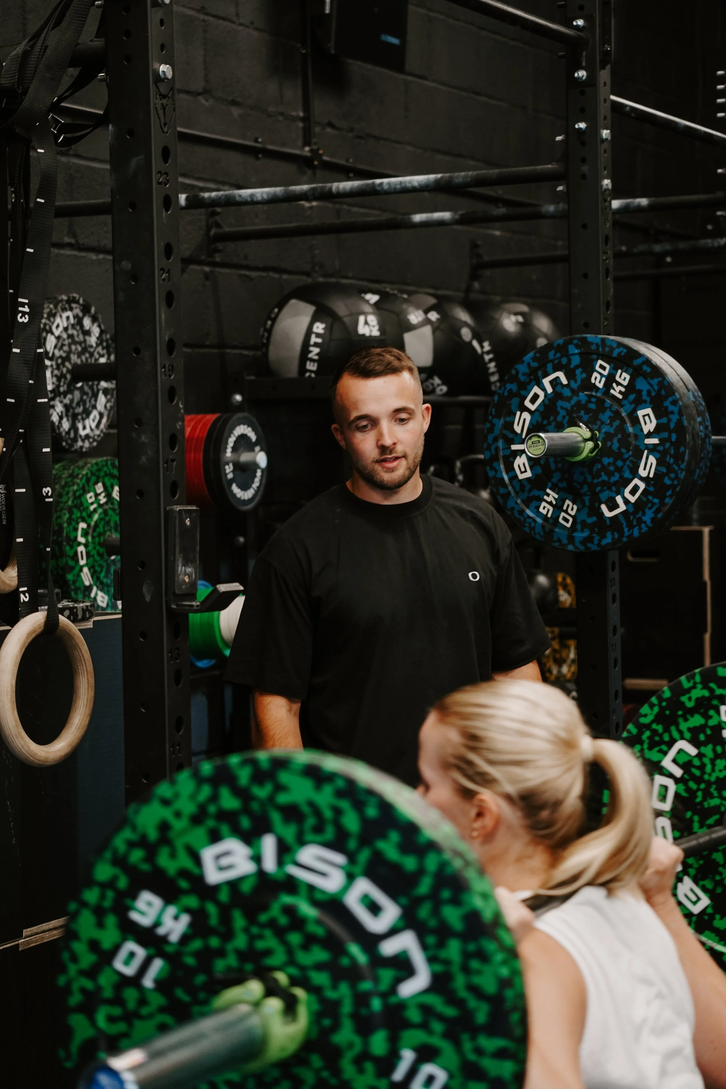 Personal trainer coaching a woman through a barbell back squat in a gym