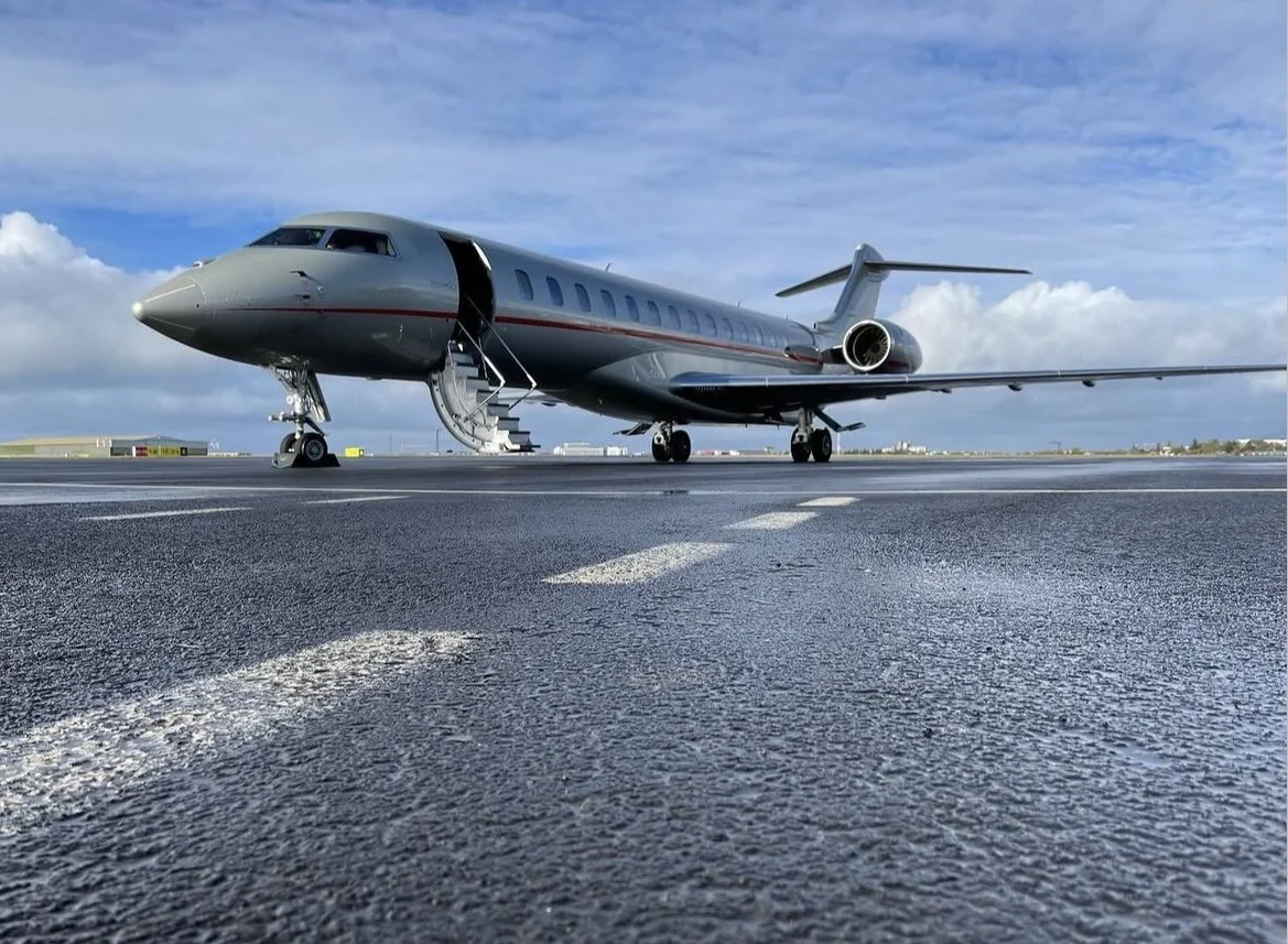 Private jet on an airport runway with stairs leading into the aircraft, under a cloudy sky.