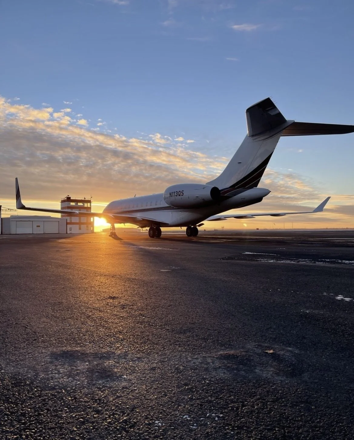Private jet parked on the tarmac during sunset with clouds in the sky.