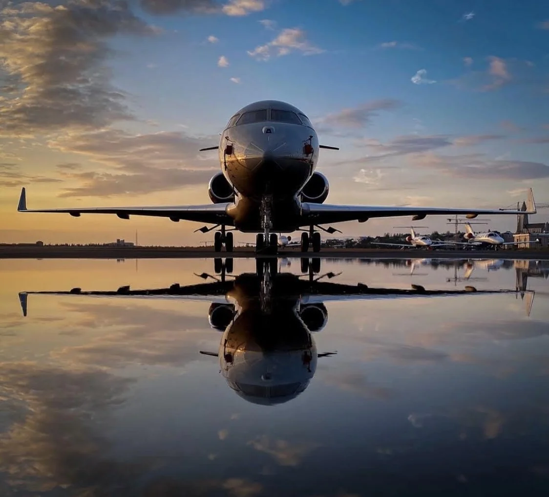 A commercial airplane on a tarmac at sunset with a reflection on wet ground.