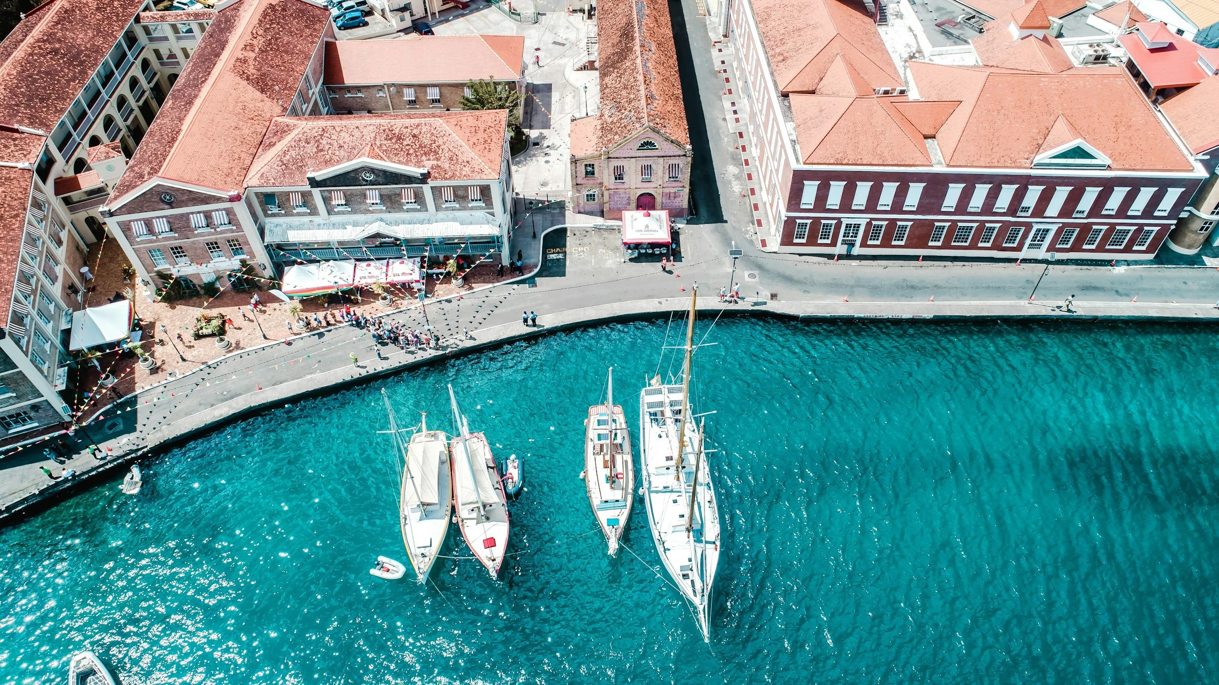 Aerial view of waterfront with boats docked and historic buildings with red tile roofs along the shoreline.