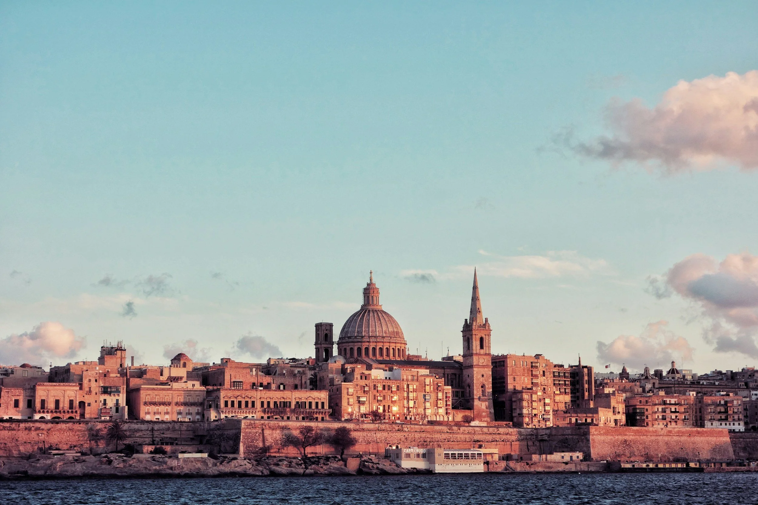 City skyline with historic buildings and churches seen from across a body of water during sunset