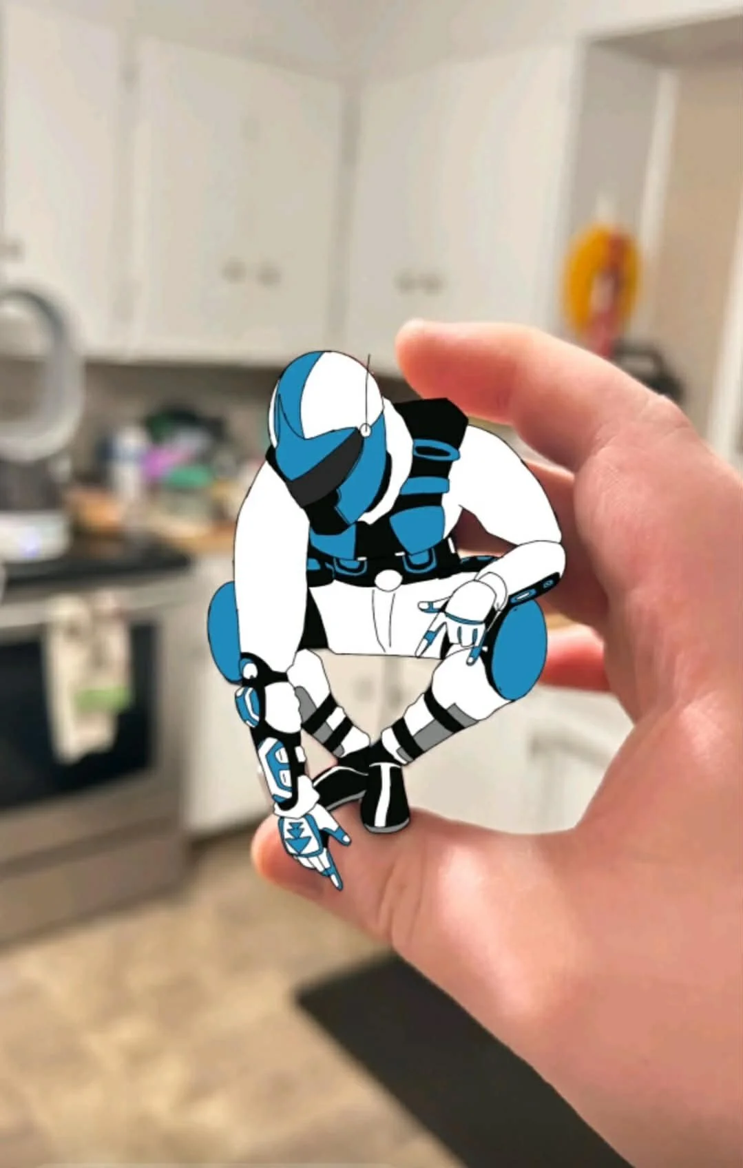 Hand holding a cartoon sticker of a futuristic soldier in a crouched position, in a kitchen background.