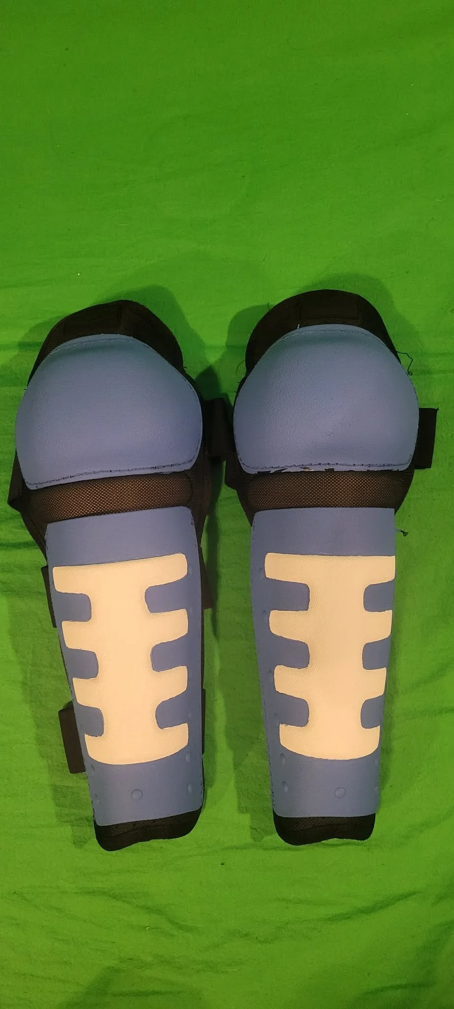 Pair of black and white shin guards with reflective accents on a green floor.