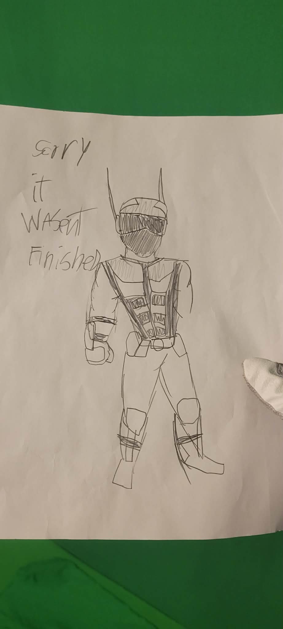 Hand-drawn sketch of a superhero character wearing a helmet and mask, with a costume featuring various straps and armor. Next to the drawing, the handwritten words say, "Sorry it wasn't finished."