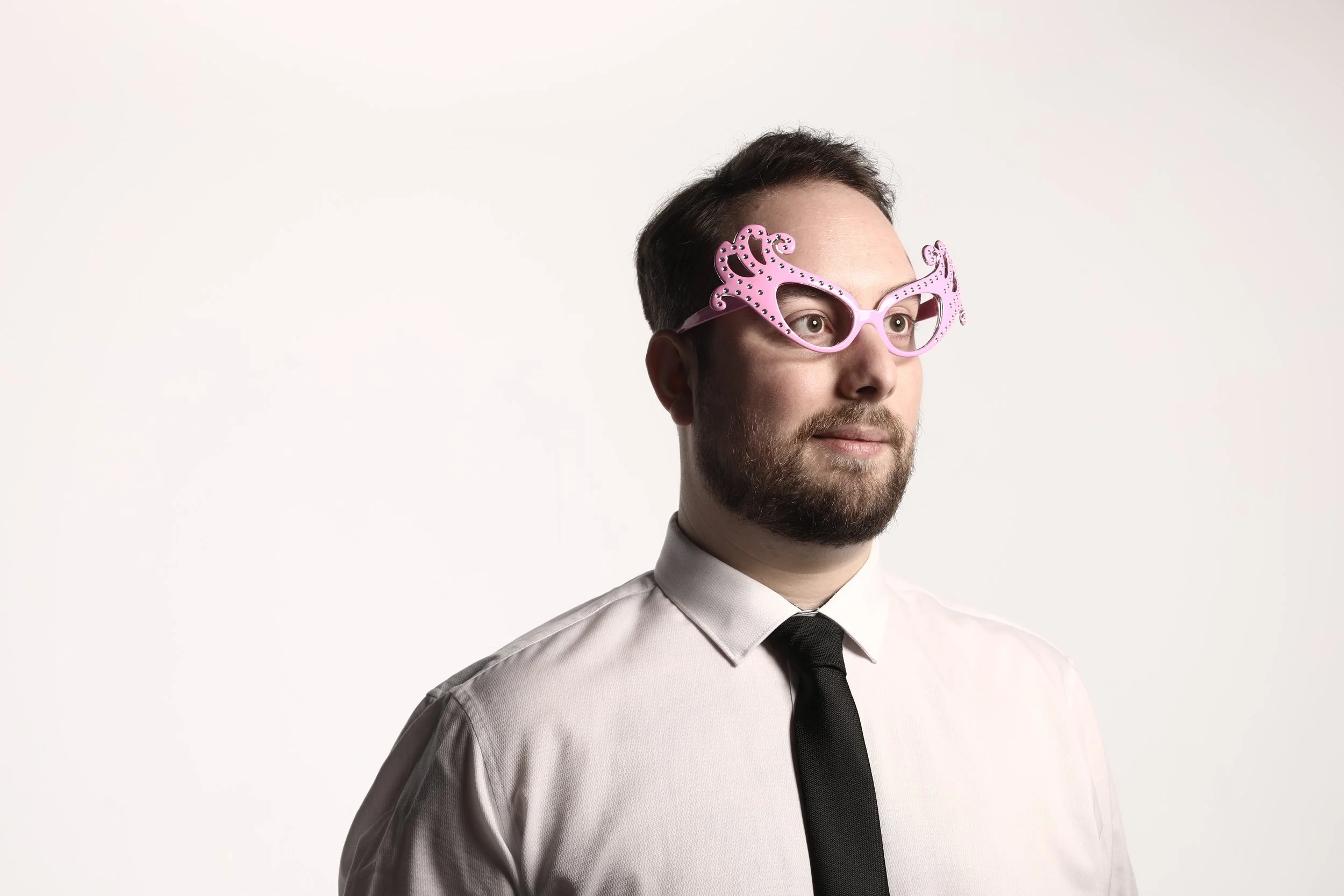 Man wearing pink novelty glasses with decorative designs, dressed in a white shirt and black tie, against a plain white background.