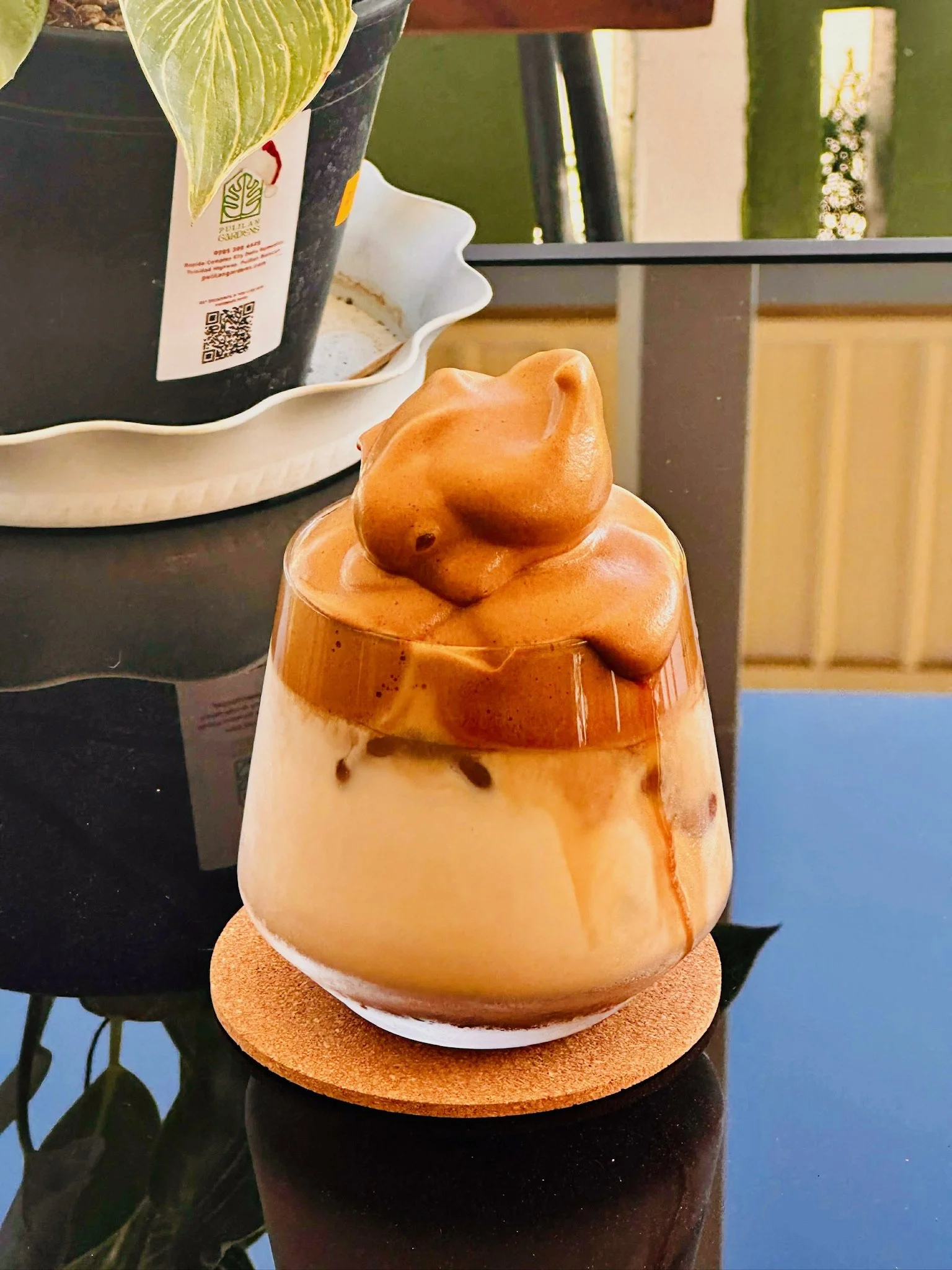 A small ceramic decorative object with a shape resembling an abstract animal head, sitting on a round base. The object has a glossy finish with swirls of brown and beige. It is placed on a dark surface.