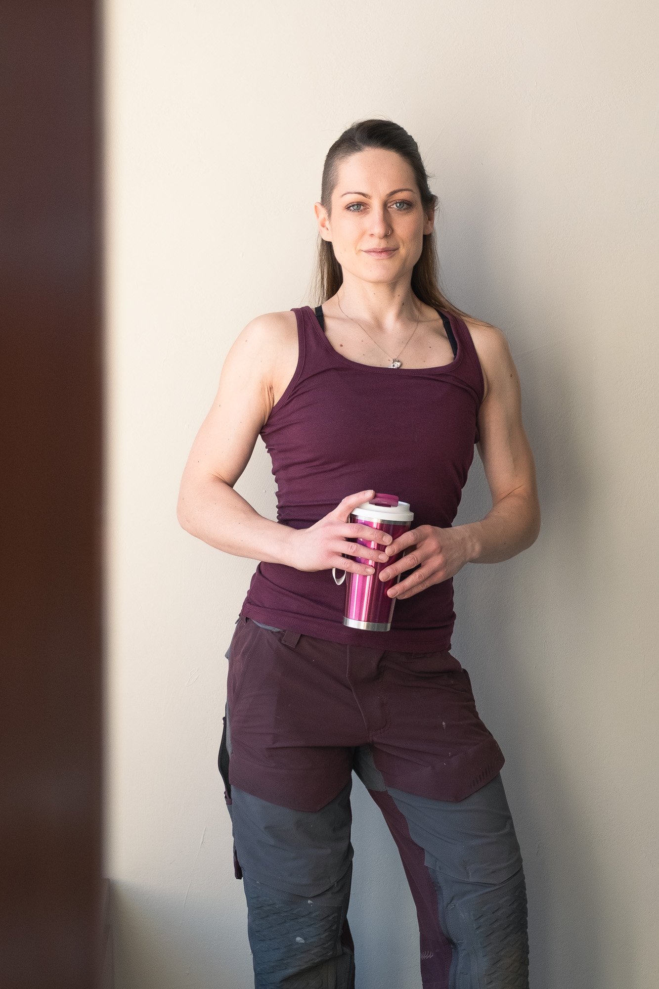 Naisyrittäjä Fanny Haddas violeteissa työvaatteissa termospullo käsissään hymyilemässä kameraa kohti.