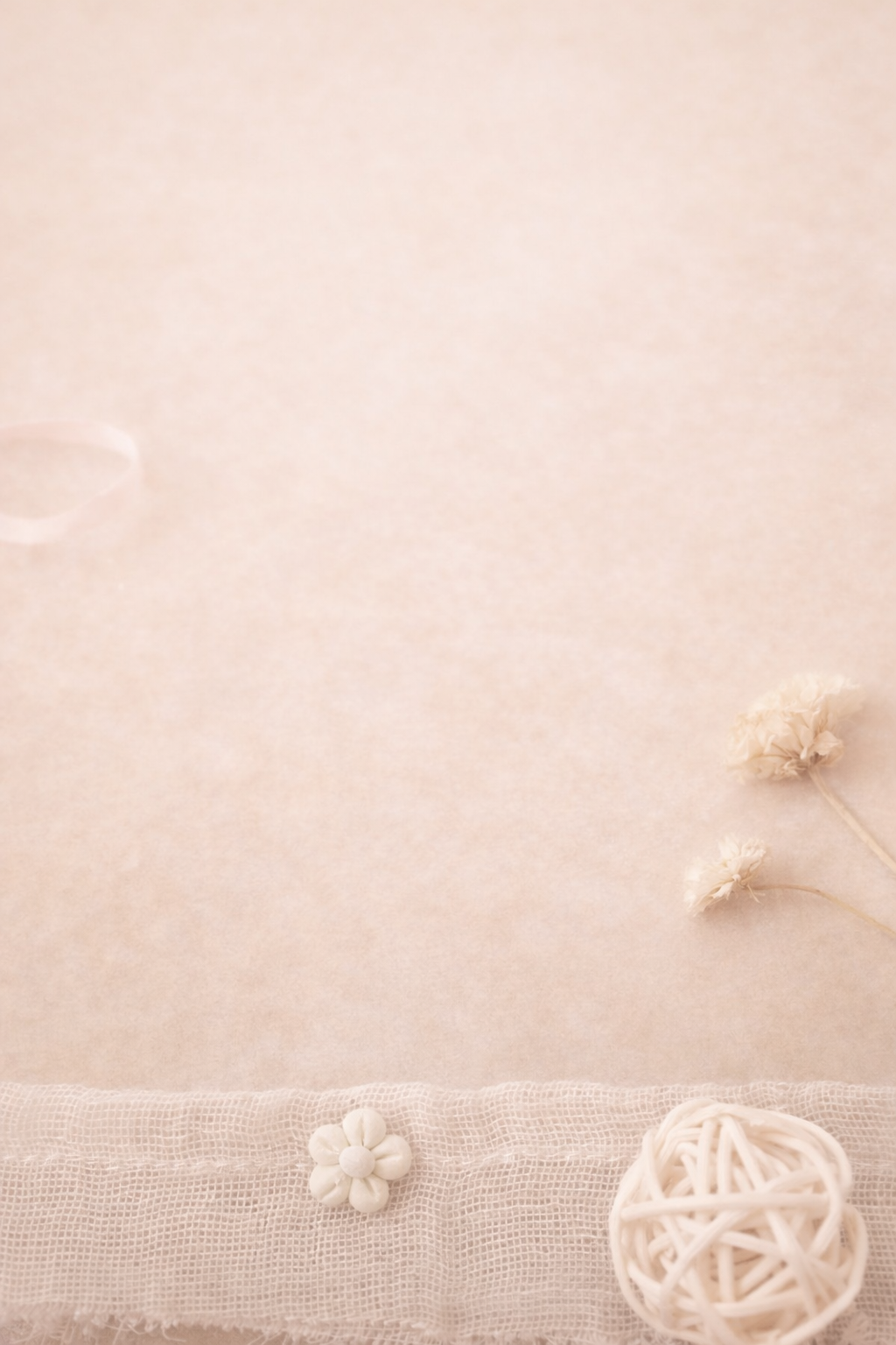 Fond beige clair avec des petits éléments décoratifs en tissu ou en corde tressée, dont une petite fleur blanche, deux autres formes rondes en forme de fleurs et un ball blanc en rotin.