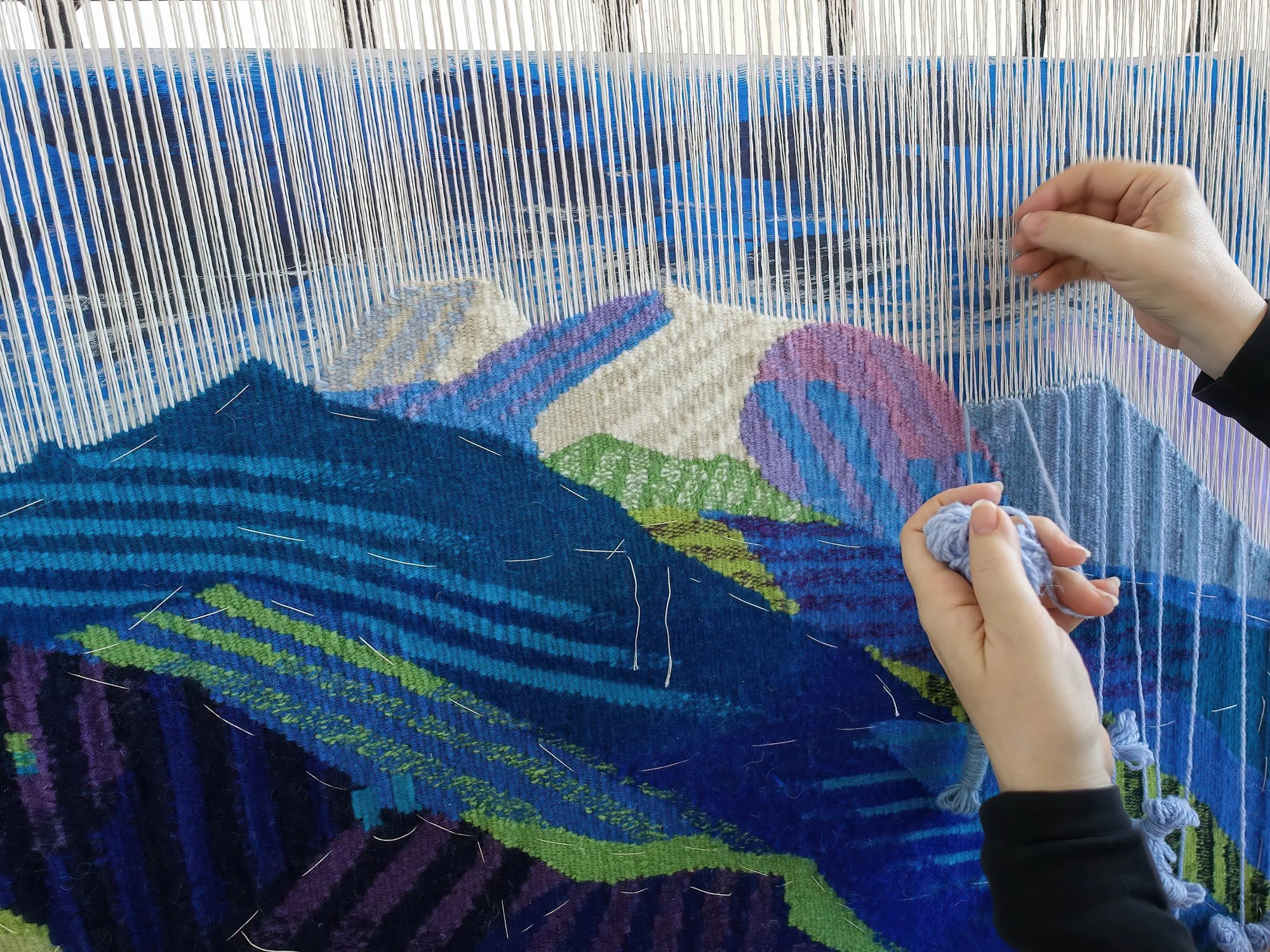 Person working on a colorful woven textile on a loom.