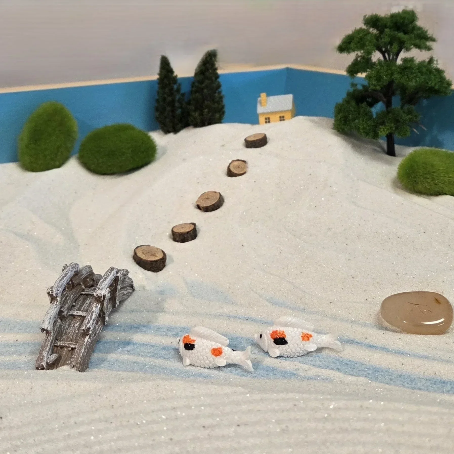 Miniature winter scene with a snow-covered landscape, small pine trees, a yellow house, a snowman, and two white ducks with orange beaks.