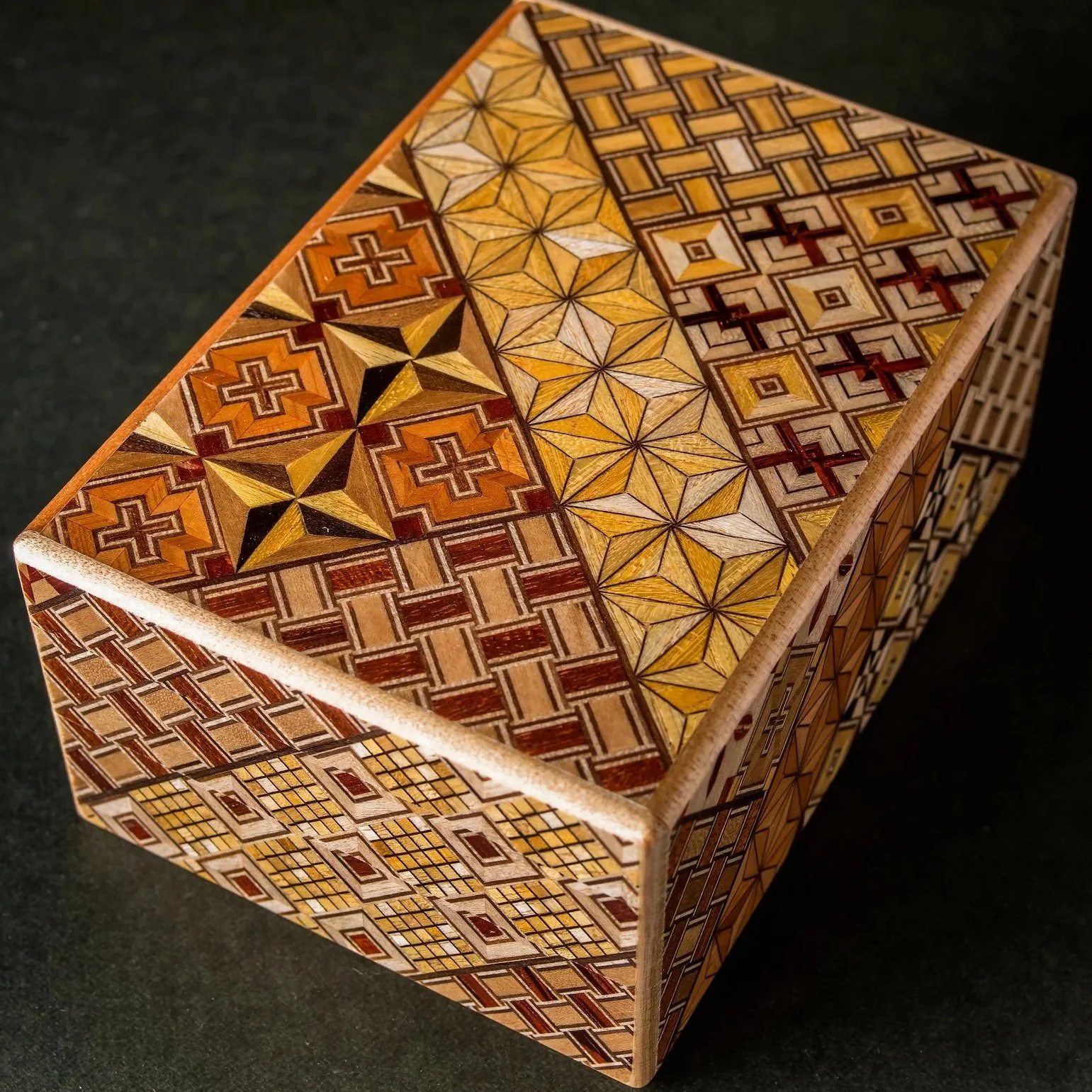 A 3D wooden box with intricate geometric patterns and designs in various shades of brown, beige, yellow, and black, covering the top and sides of the box.