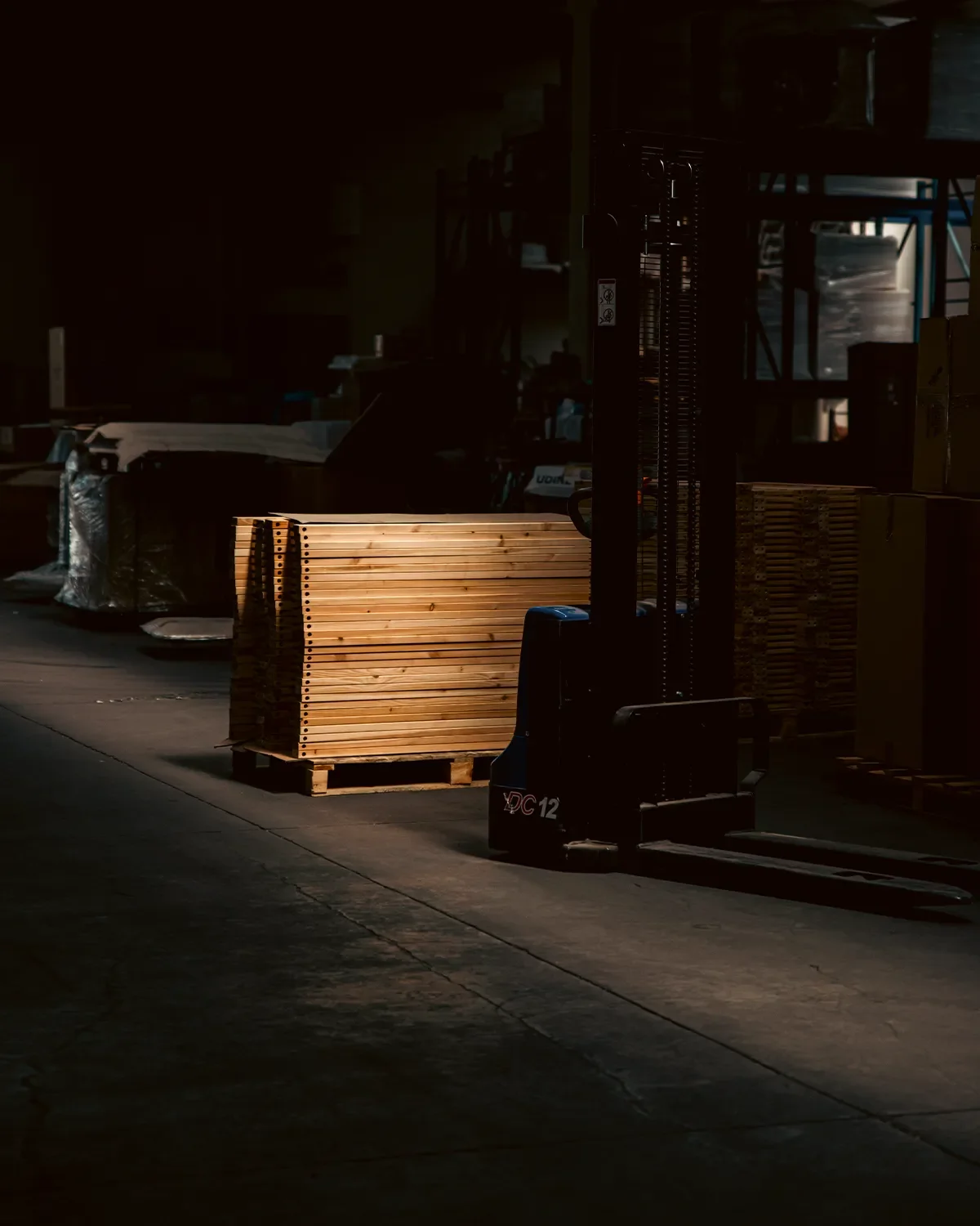Pallet di legno in un magazzino con luci soffuse e una scala aerea sullo sfondo.