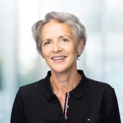 Smiling woman with grey hair wearing a black jacket in a bright, modern indoor setting