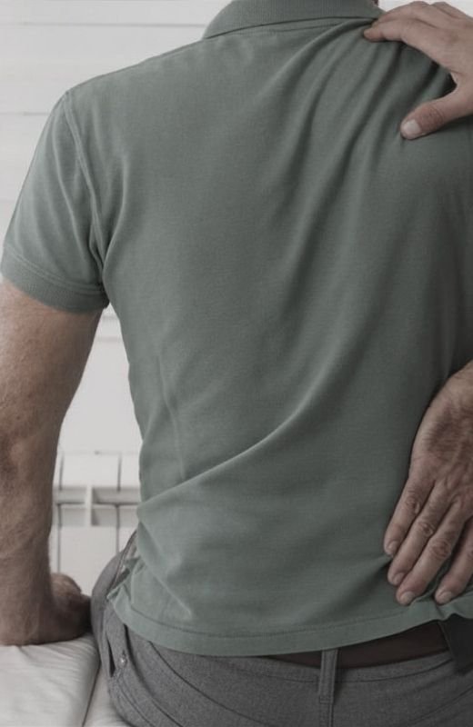 A person is touching their lower back with one hand while leaning slightly forward.
