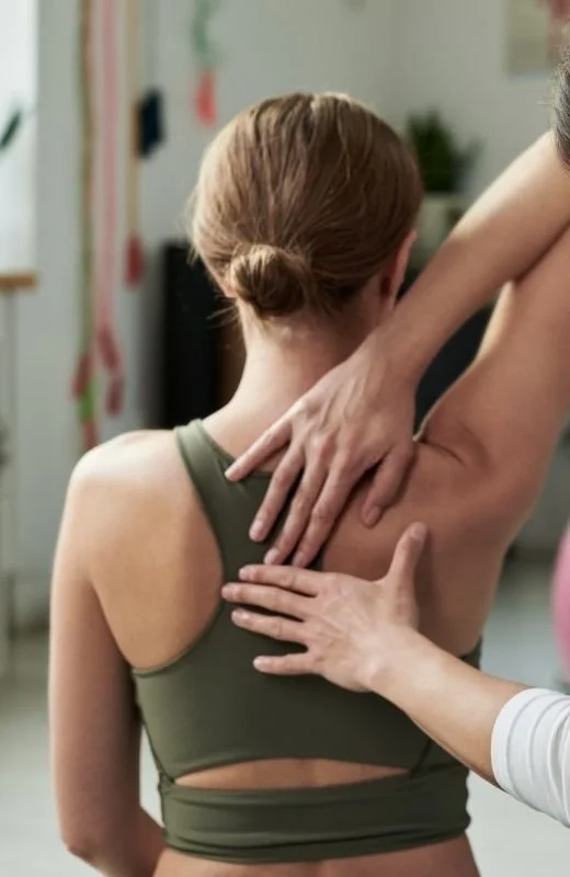 A person with brown hair in a bun is receiving an Amatsu therapy shoulder adjustment from a healthcare professional in a clinical setting.