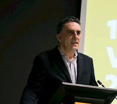 A man speaking at a lectern during a presentation or conference.