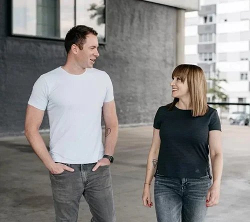 A man and a woman walking and smiling at each other outdoors in an urban area.