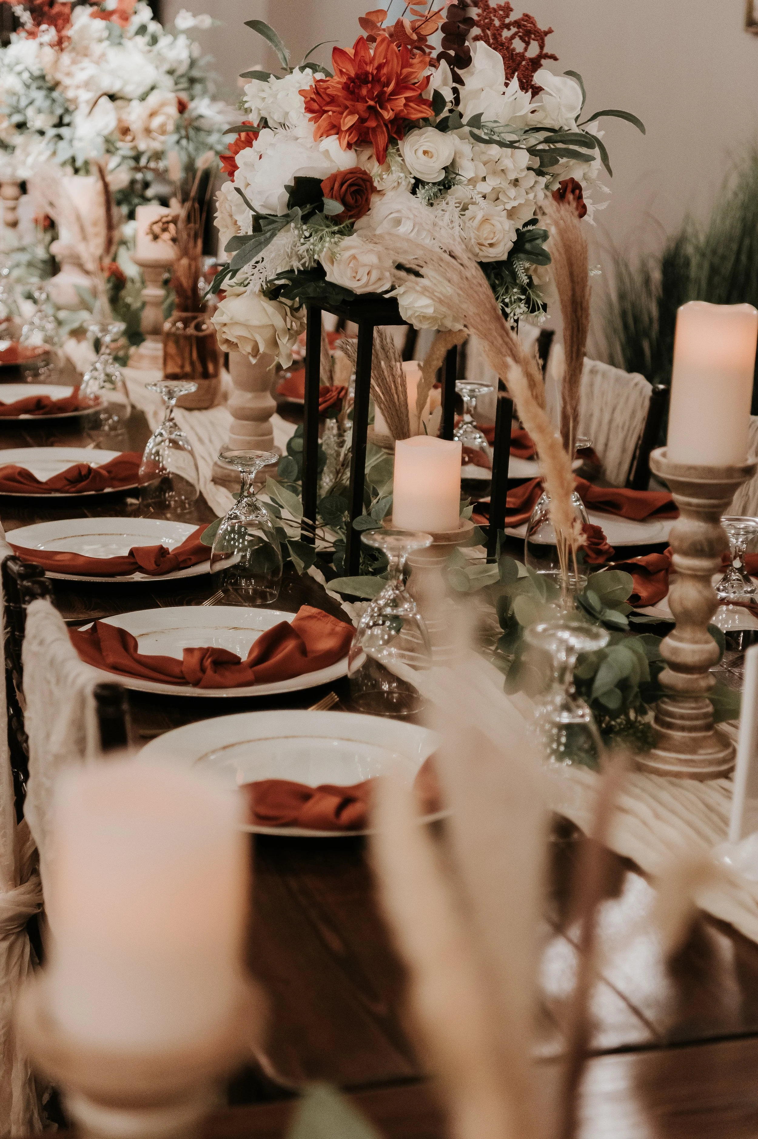 A decorated banquet table with candles, floral arrangements, and place settings with orange napkins.