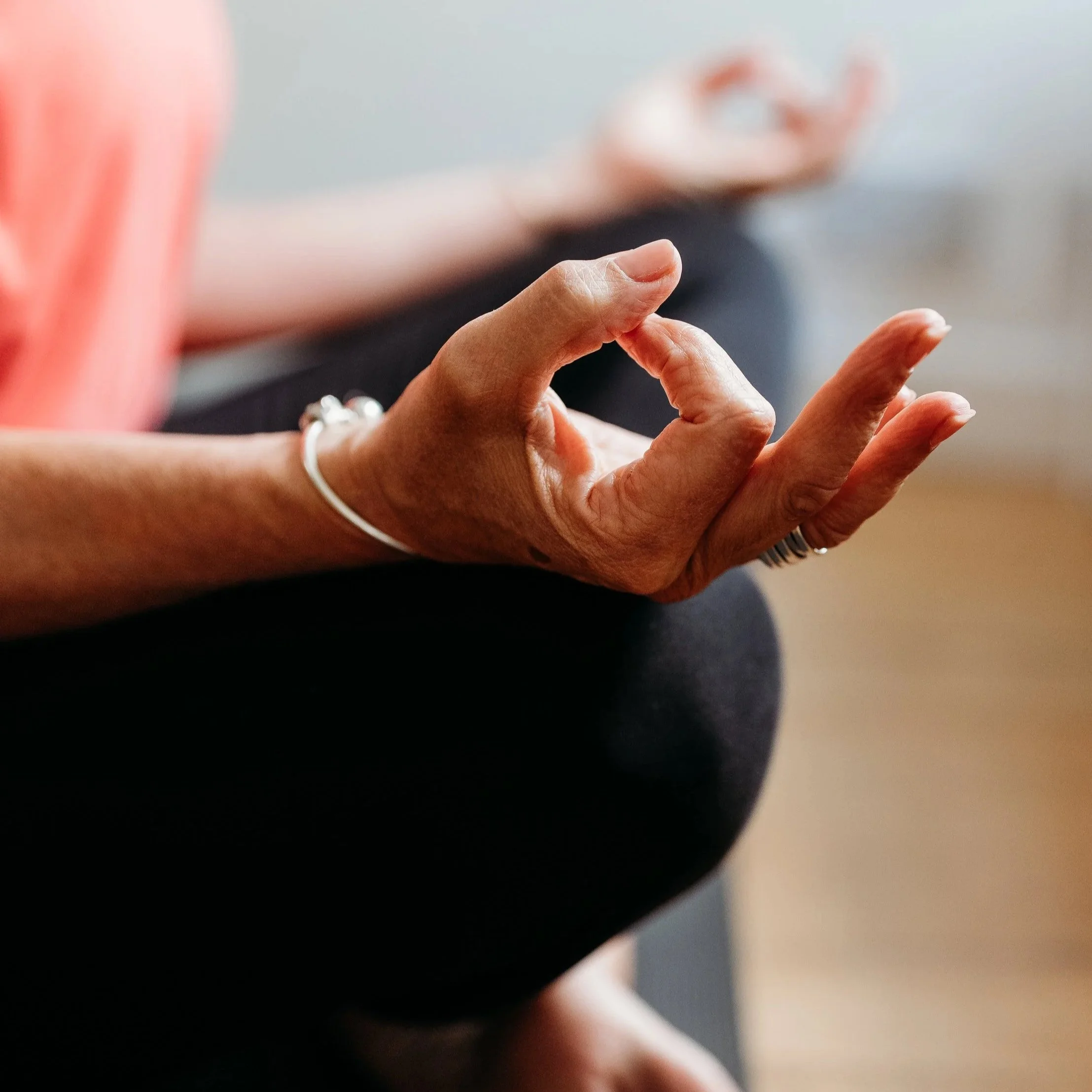 Louise from the healing mat sitting cross-legged in a yoga pose with their hand making a mudra gesture. Louise invites you to discover yoga therapy and its benefits as a therapeutic model.