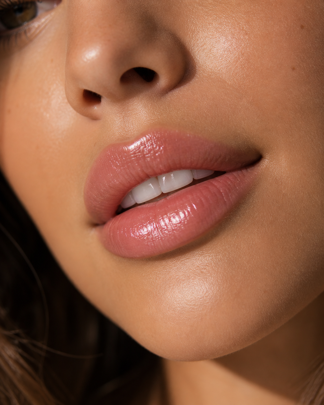 Close-up of a woman's face focusing on her lips, nose, and a partial view of her eye. She has smooth skin, full lips with gloss, and white teeth visible.
