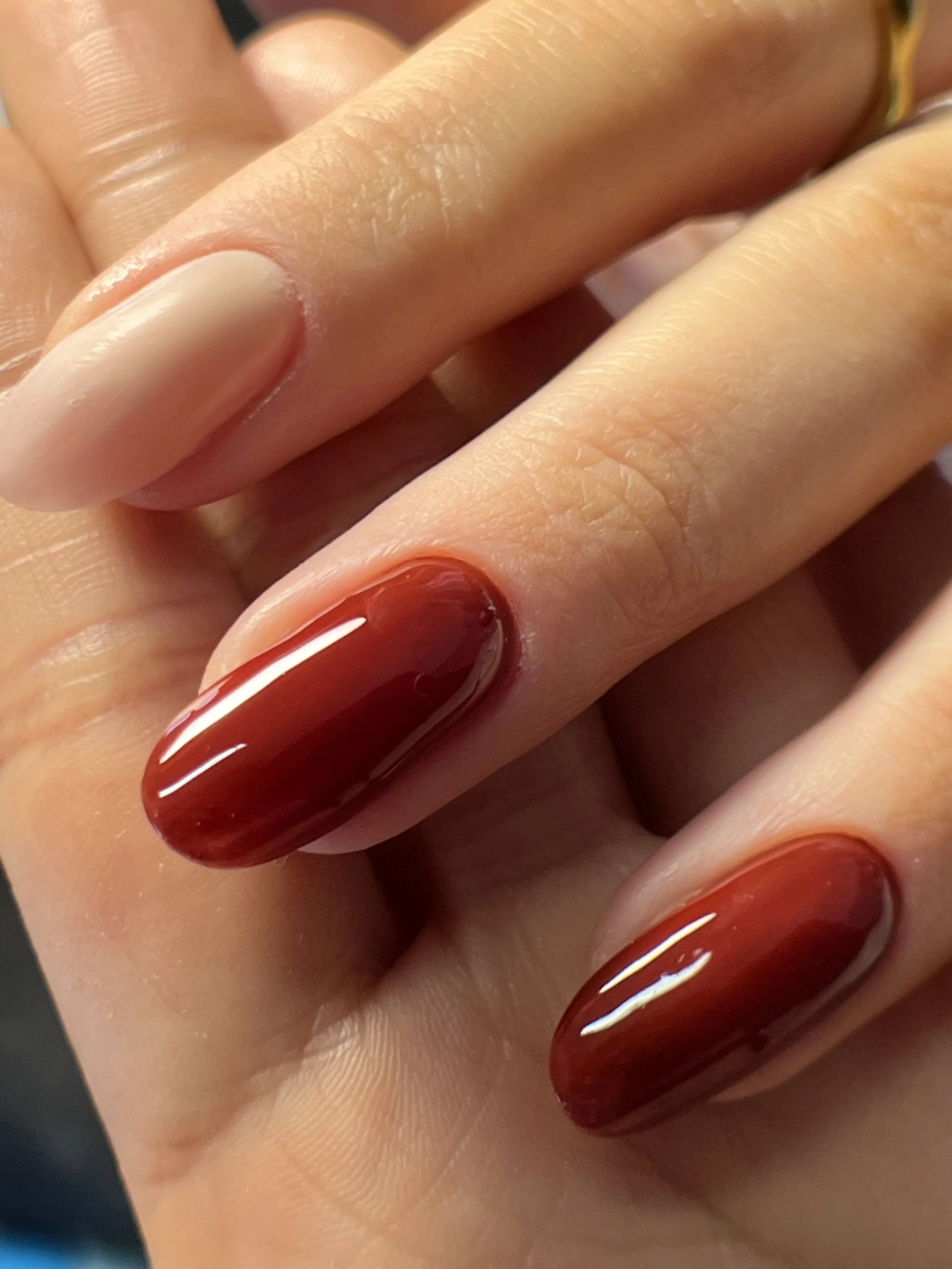 Close-up of a hand with long, oval-shaped nails painted in a glossy, gradient red and brown nail polish.