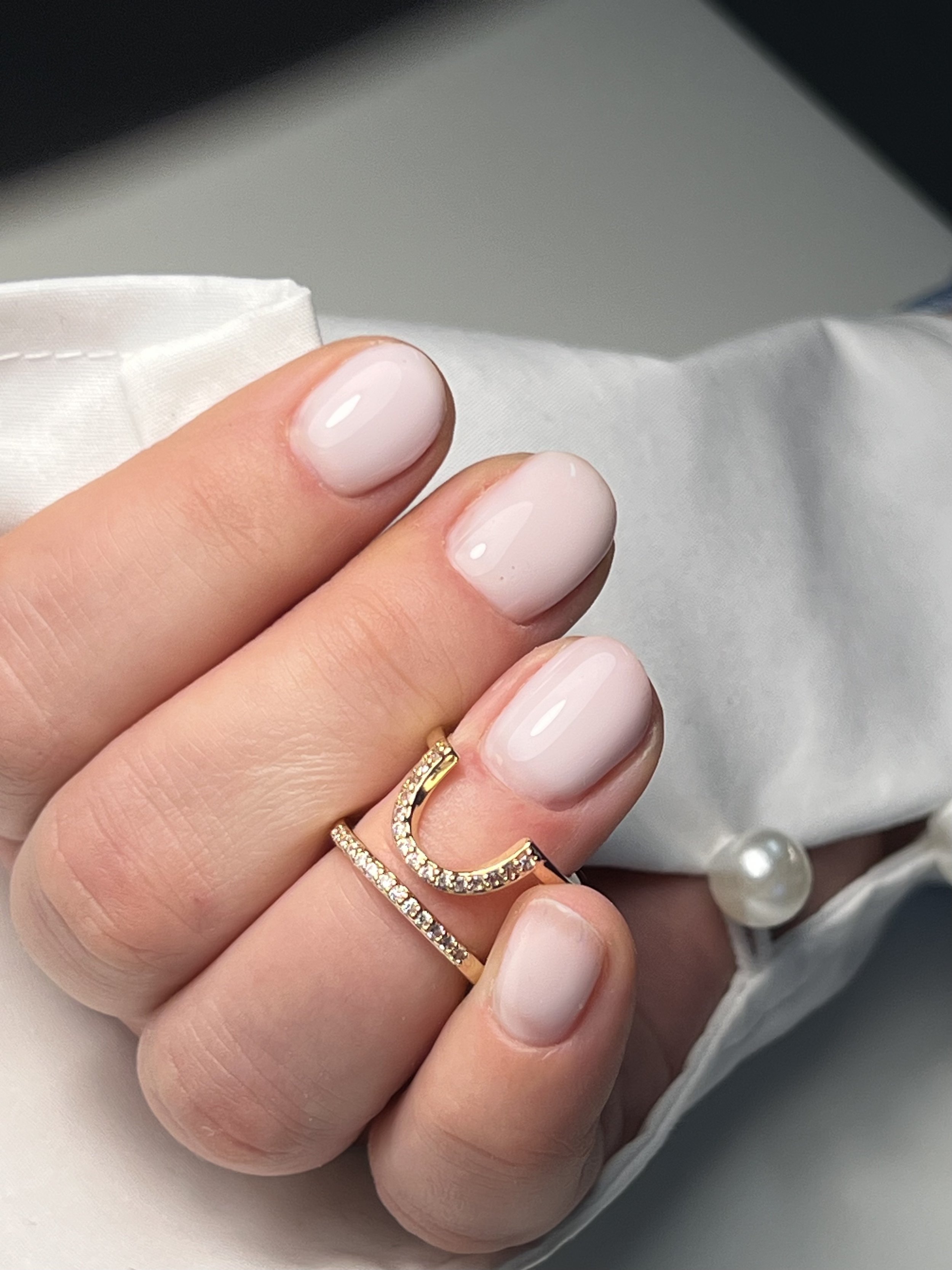 Hand with manicured nails wearing two gold rings with diamonds, against a white shirt cuff.