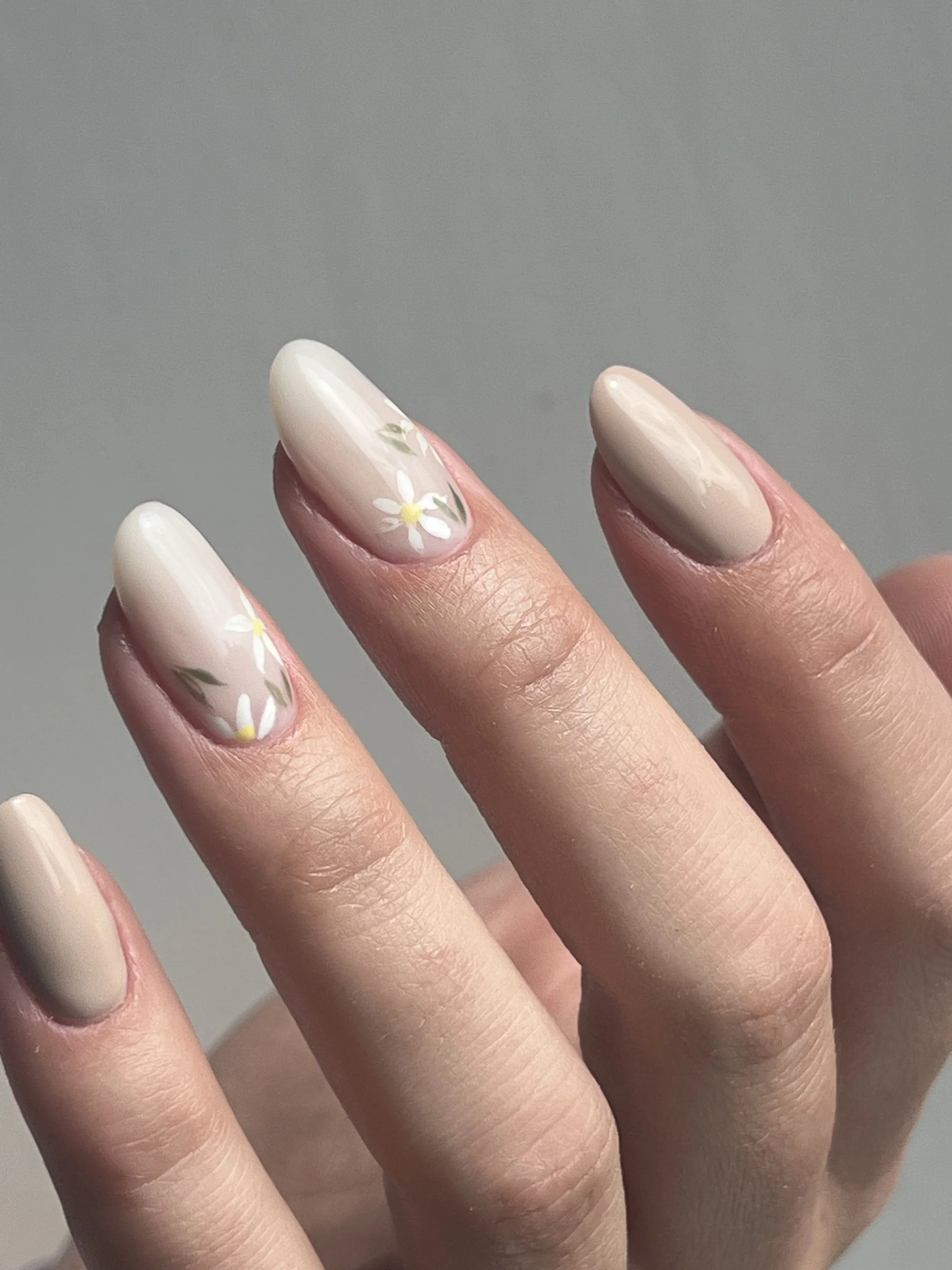 Close-up of a hand with beige nail polish and white daisy flower designs on some nails.