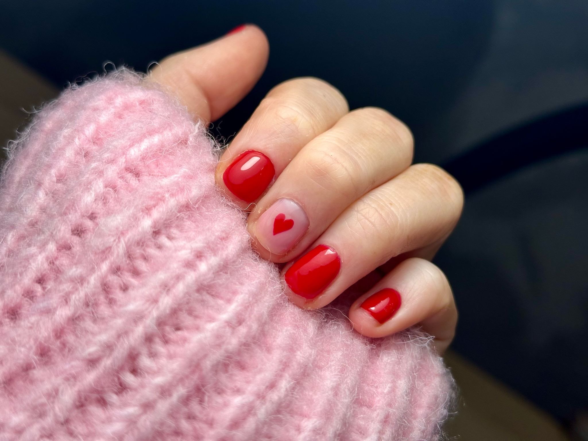 Close-up of a hand with red and pink nail polish, wearing a pink fuzzy sweater, holding the sweater.
