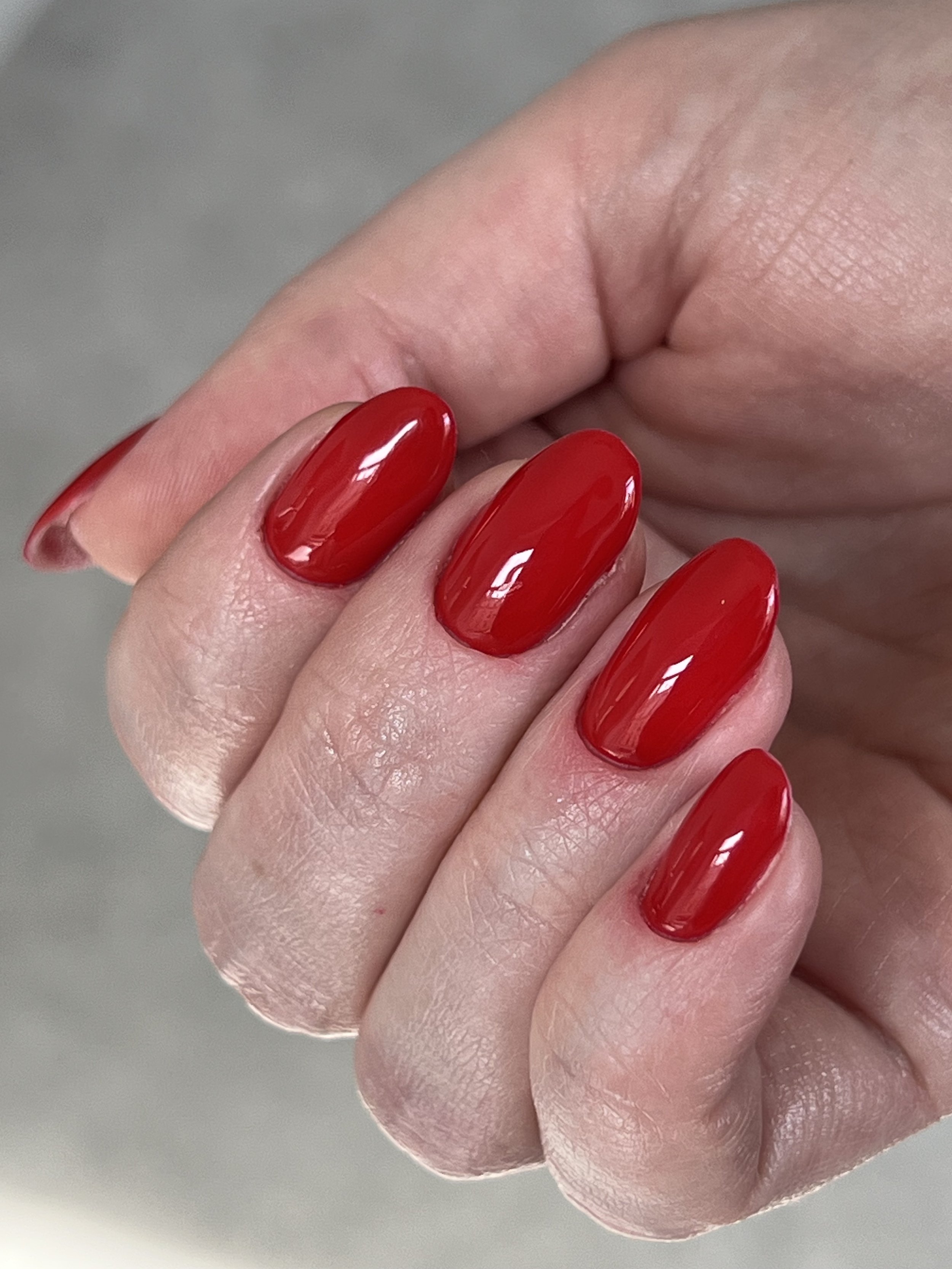 Close-up of a hand with four fingers showing, featuring red, glossy, oval-shaped manicured nails.