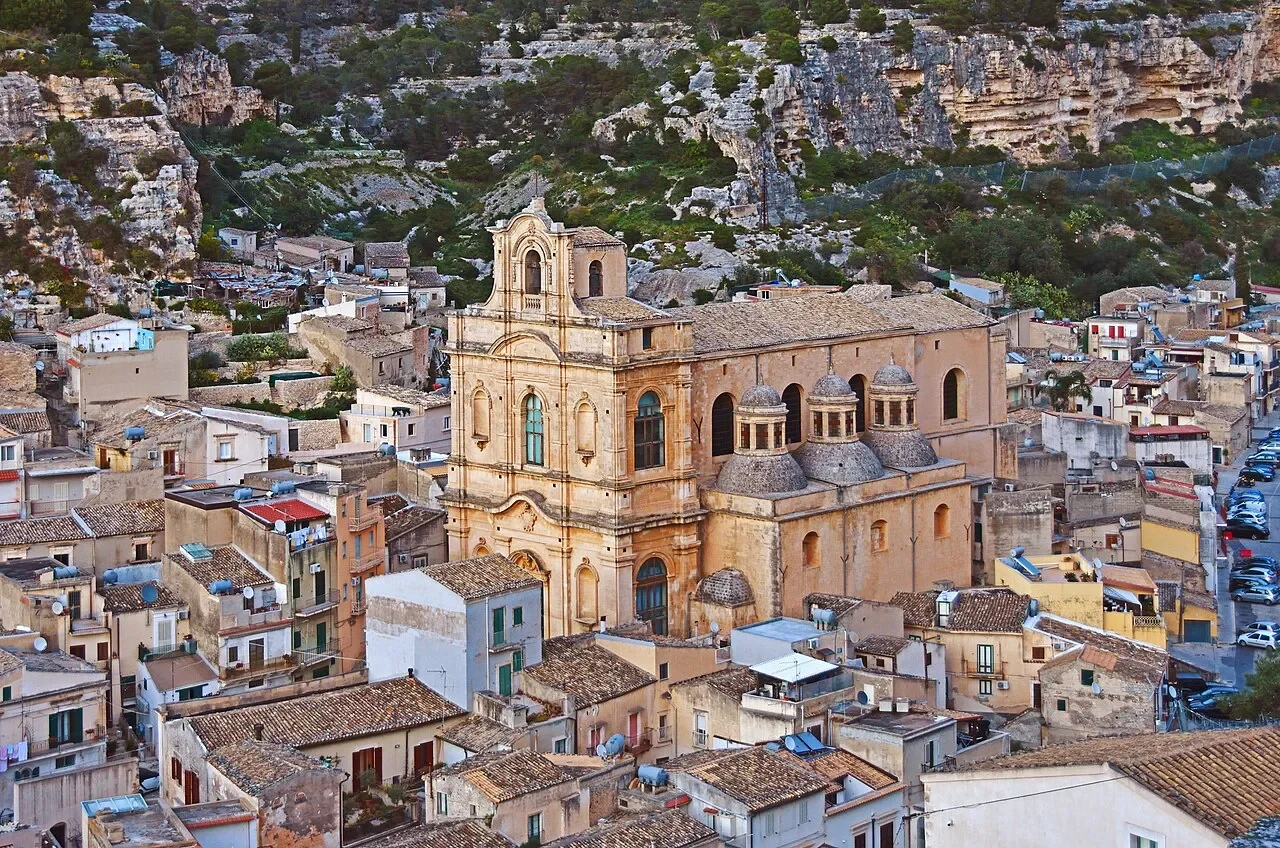 Santa Maria La Nova rising above the tiled rooftops of Scicli, beneath a rocky hillside