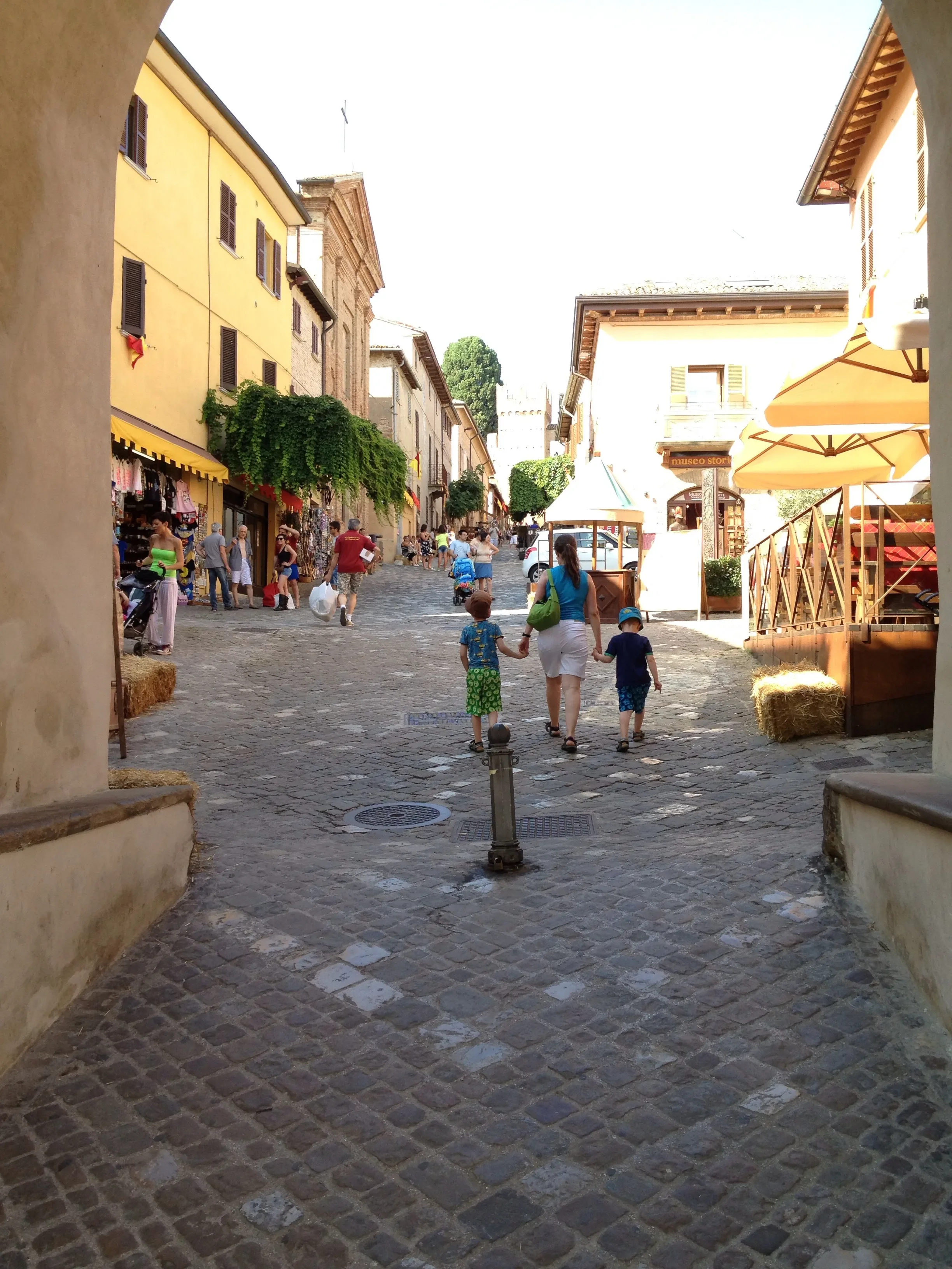 Visitors walking uphill along a cobbled street lined with shops and cafés in Gradara