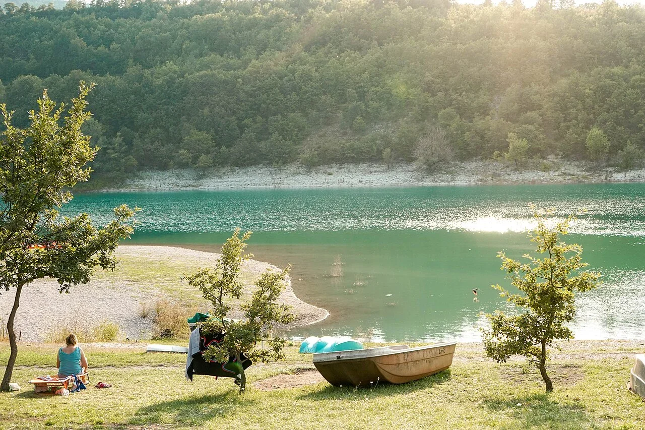 A rowing boat and visitors resting on the grassy shore of Lago di Fiastra