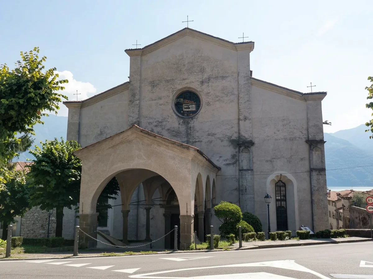 Church façade with a round window and an arched entrance porch beside a sunlit street.