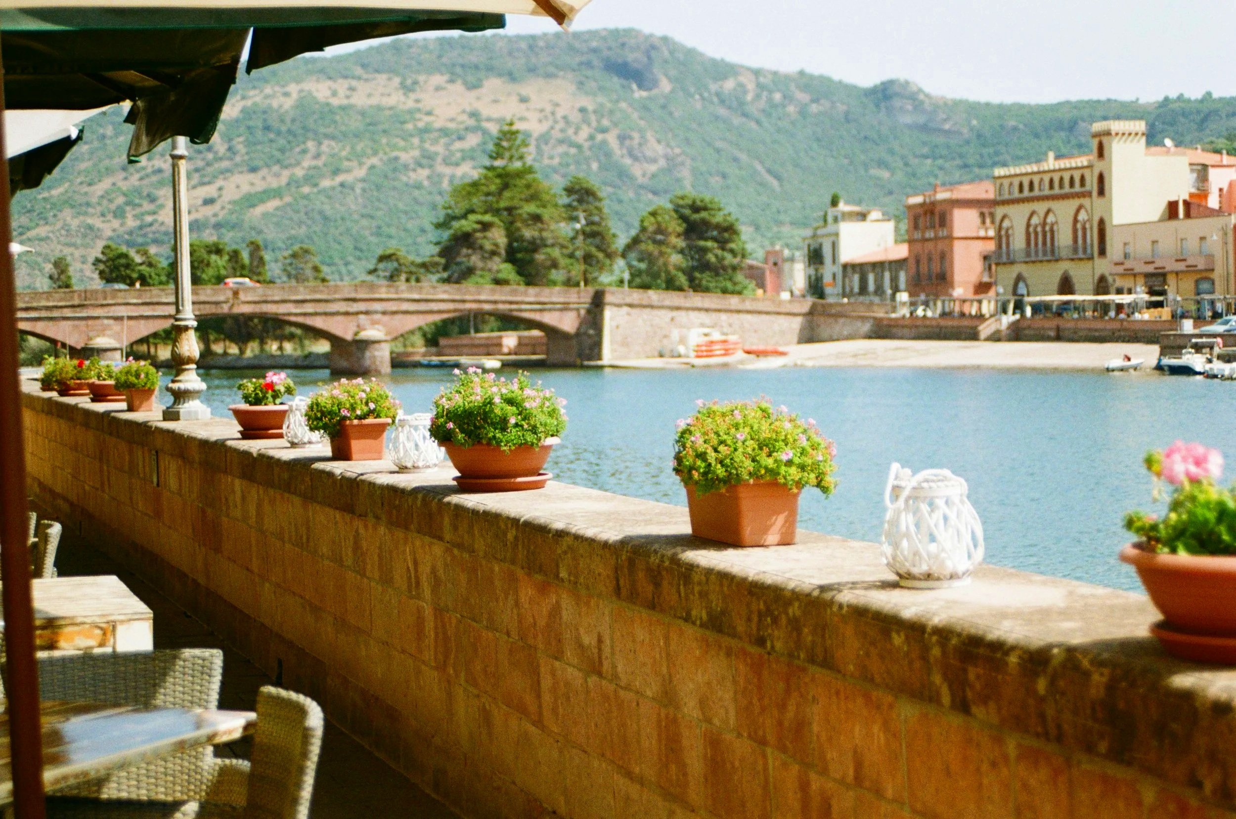 Waterfront promenade in Sardinia with colourful buildings, potted plants and a rugged mountain backdrop