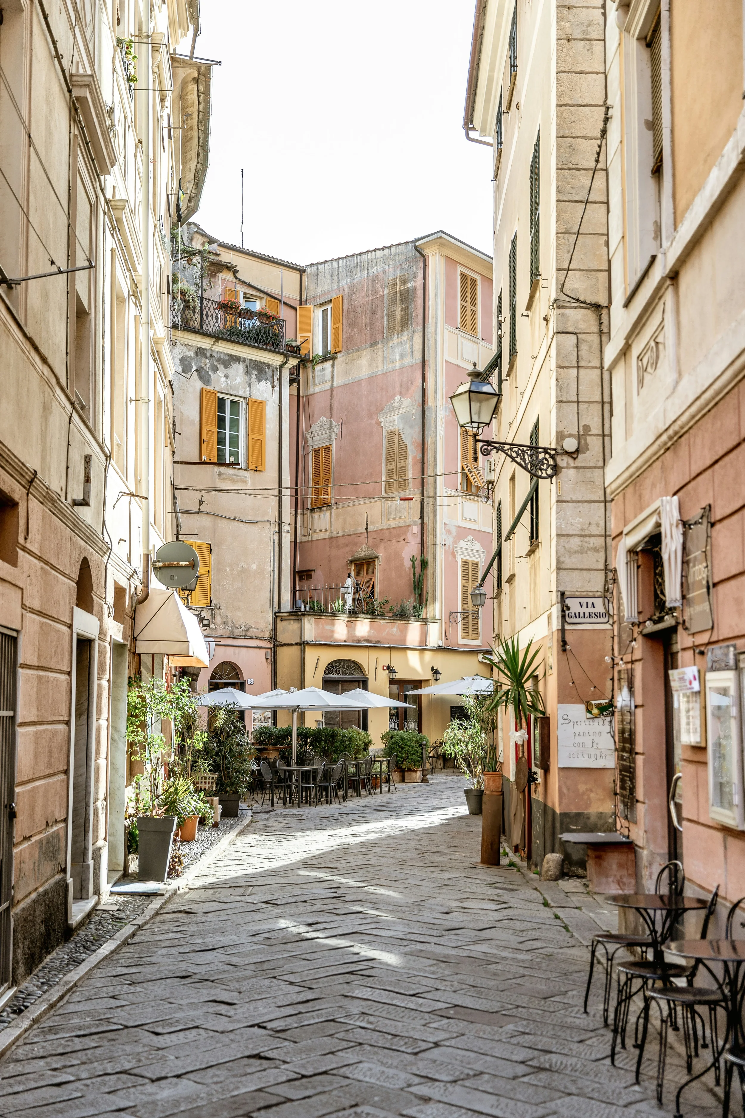 Outdoor café tables and pastel façades along a cobbled street in Finalborgo, Liguria