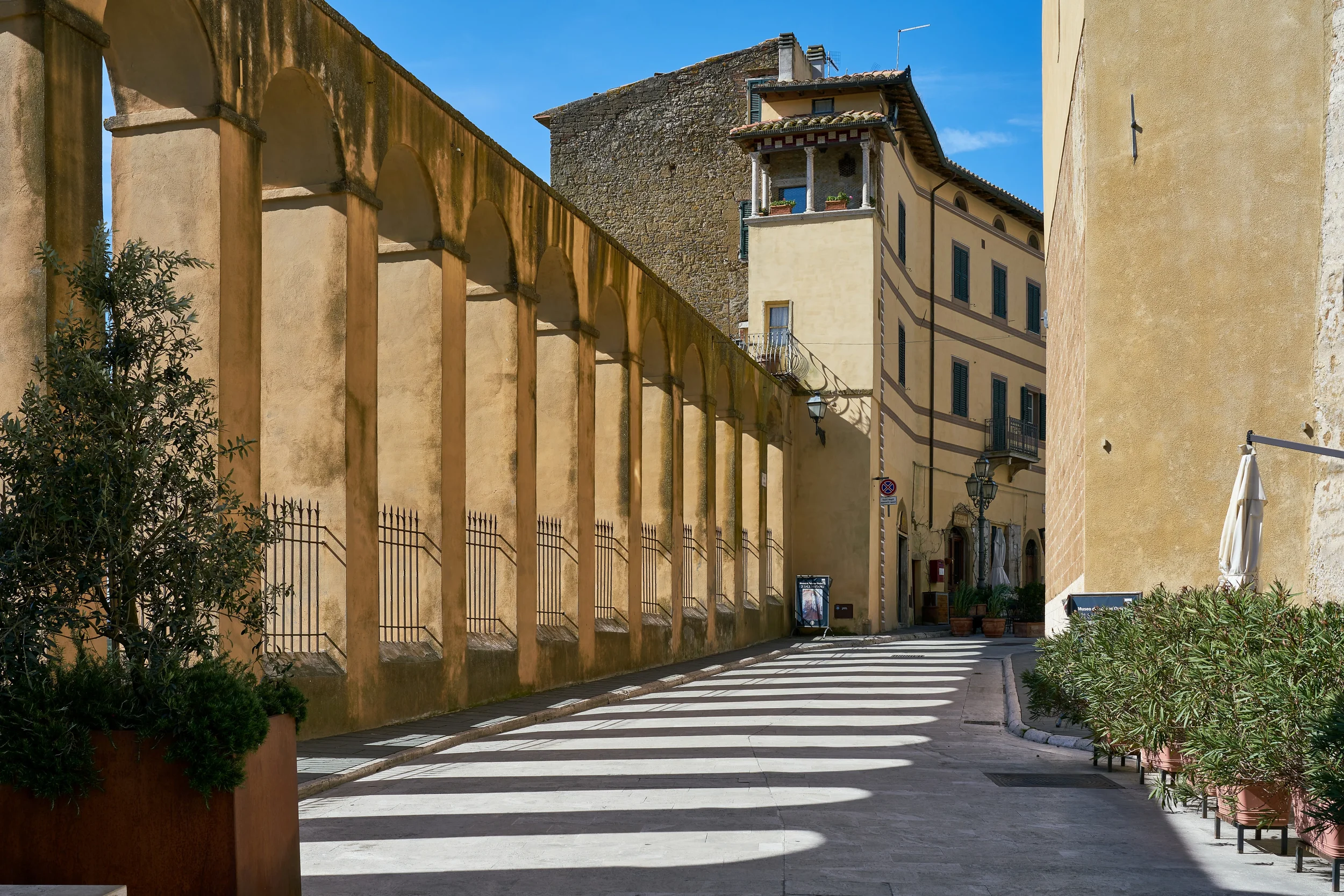 Arches of the Medici aqueduct casting striped shadows along Via Cavour in Pitigliano.