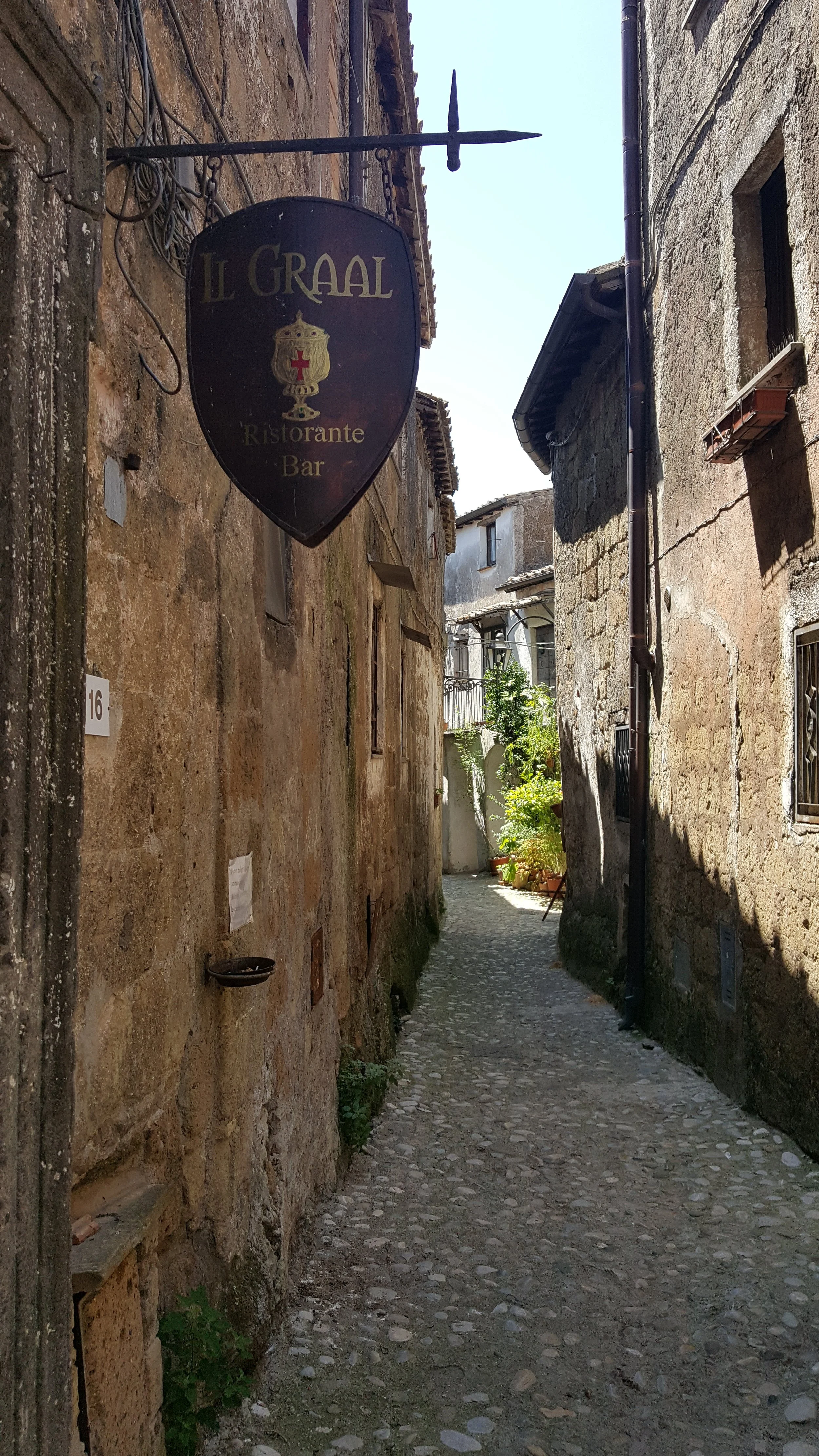 A narrow cobbled lane between stone houses beneath the Il Graal sign in Calcata Vecchia.