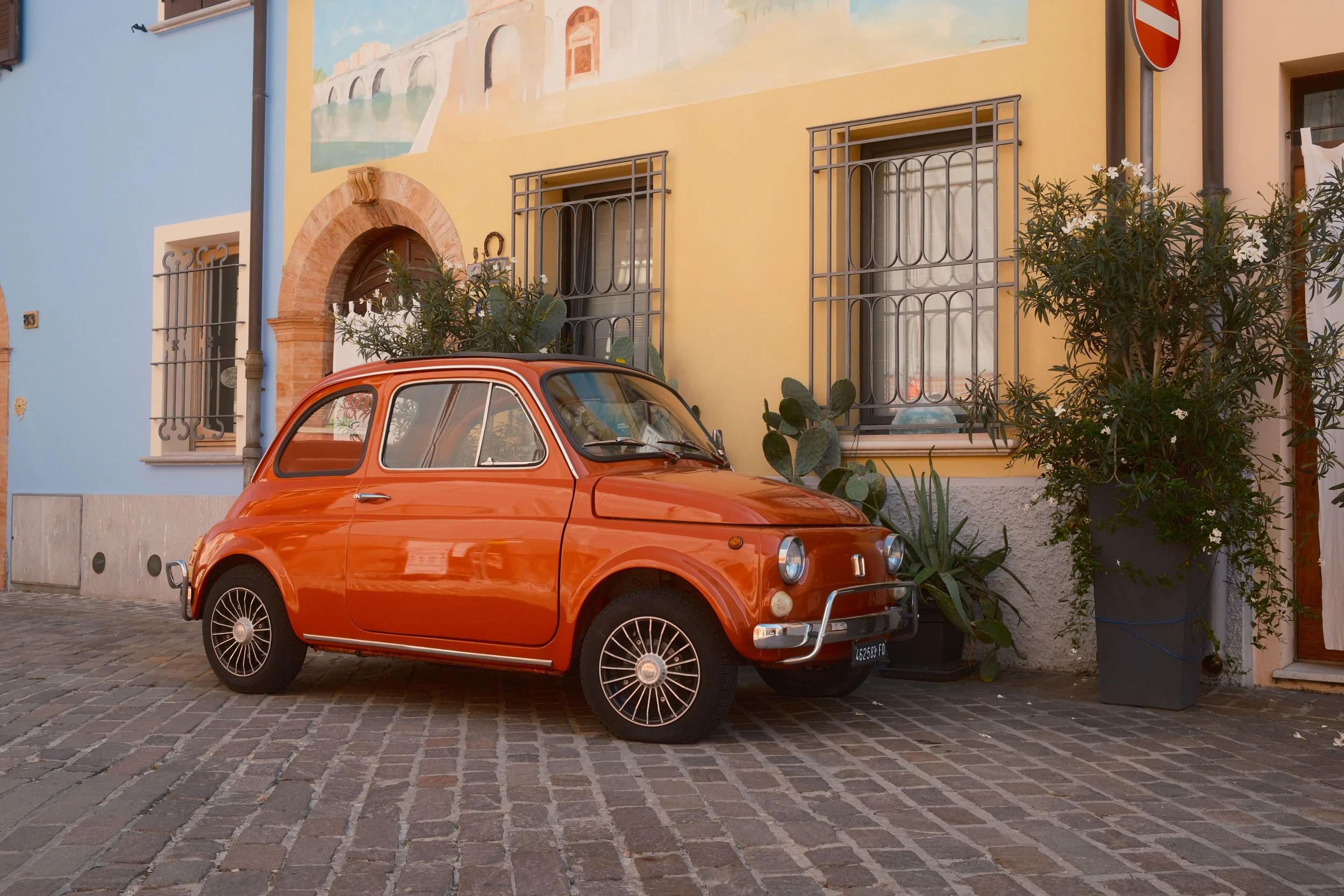 Vintage orange Fiat 500 parked beside colourful buildings on a street in southern Italy
