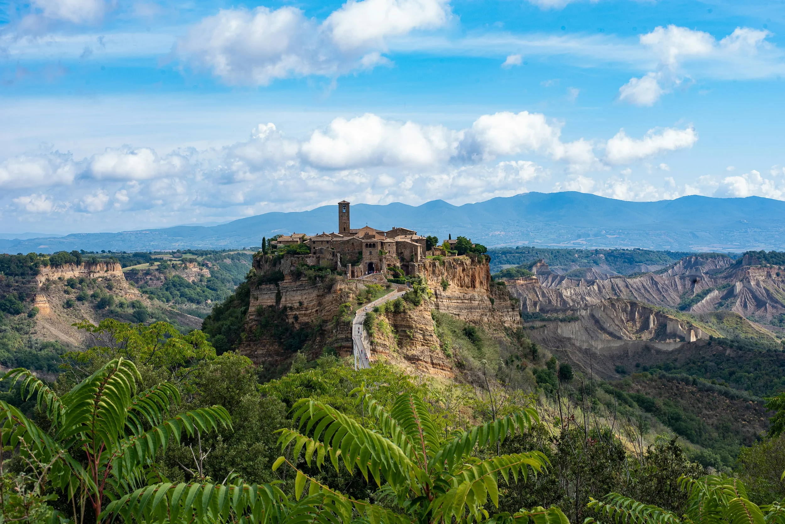 Civita di Bagnoregio on its steep tuff ridge, reached by a footbridge above the green valley and eroded clay hills.