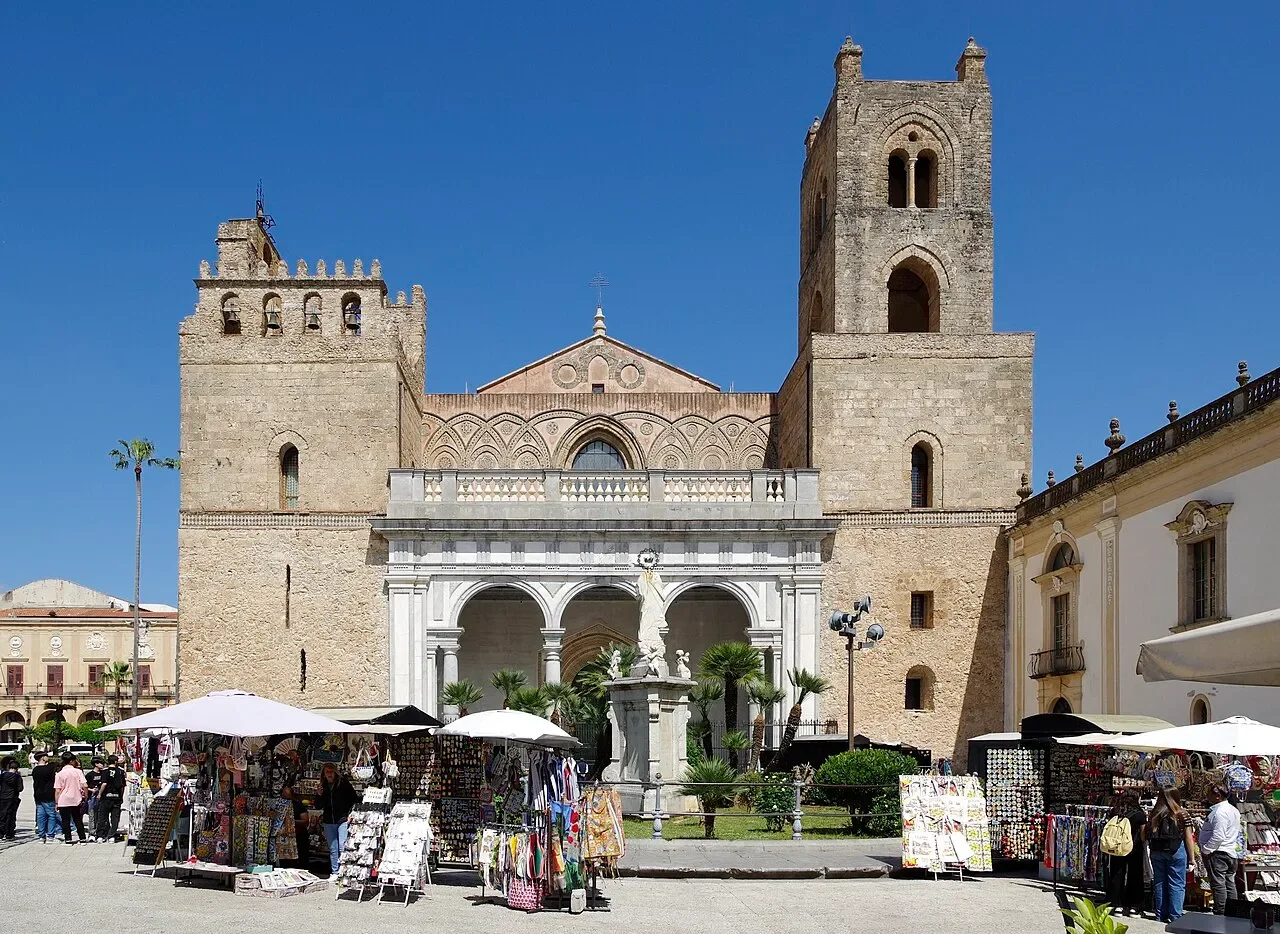 The twin towers and columned entrance of Monreale Cathedral, with market stalls in the square