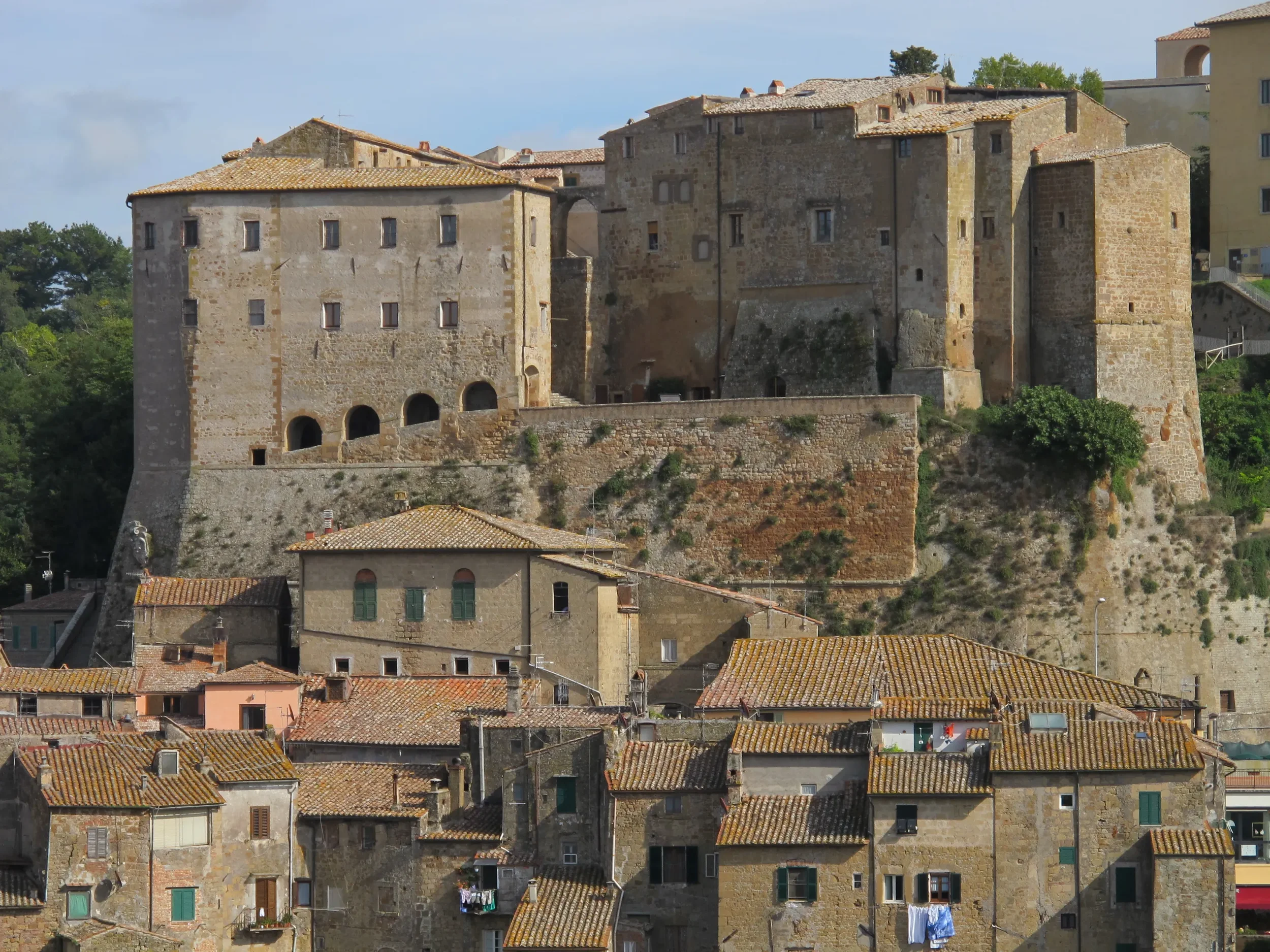 The stone walls and buildings of Fortezza Orsini rising above the tiled rooftops of Sorano.