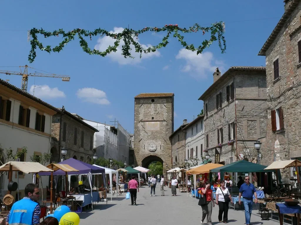 Market stalls in Piazza Garibaldi leading towards the stone Porta Cannara gateway in Bevagna