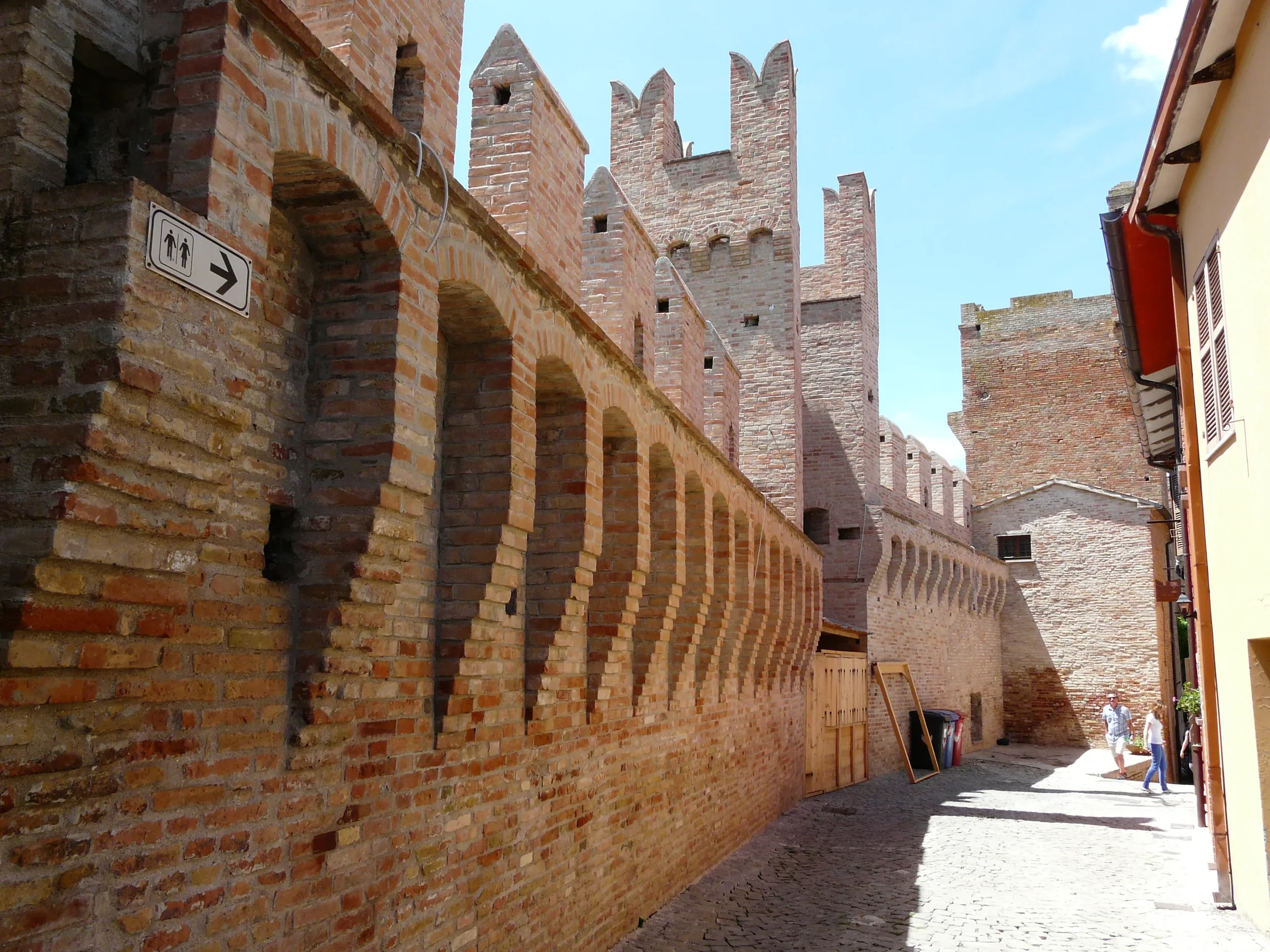 Narrow village lane running beside the tall brick ramparts and towers of Gradara