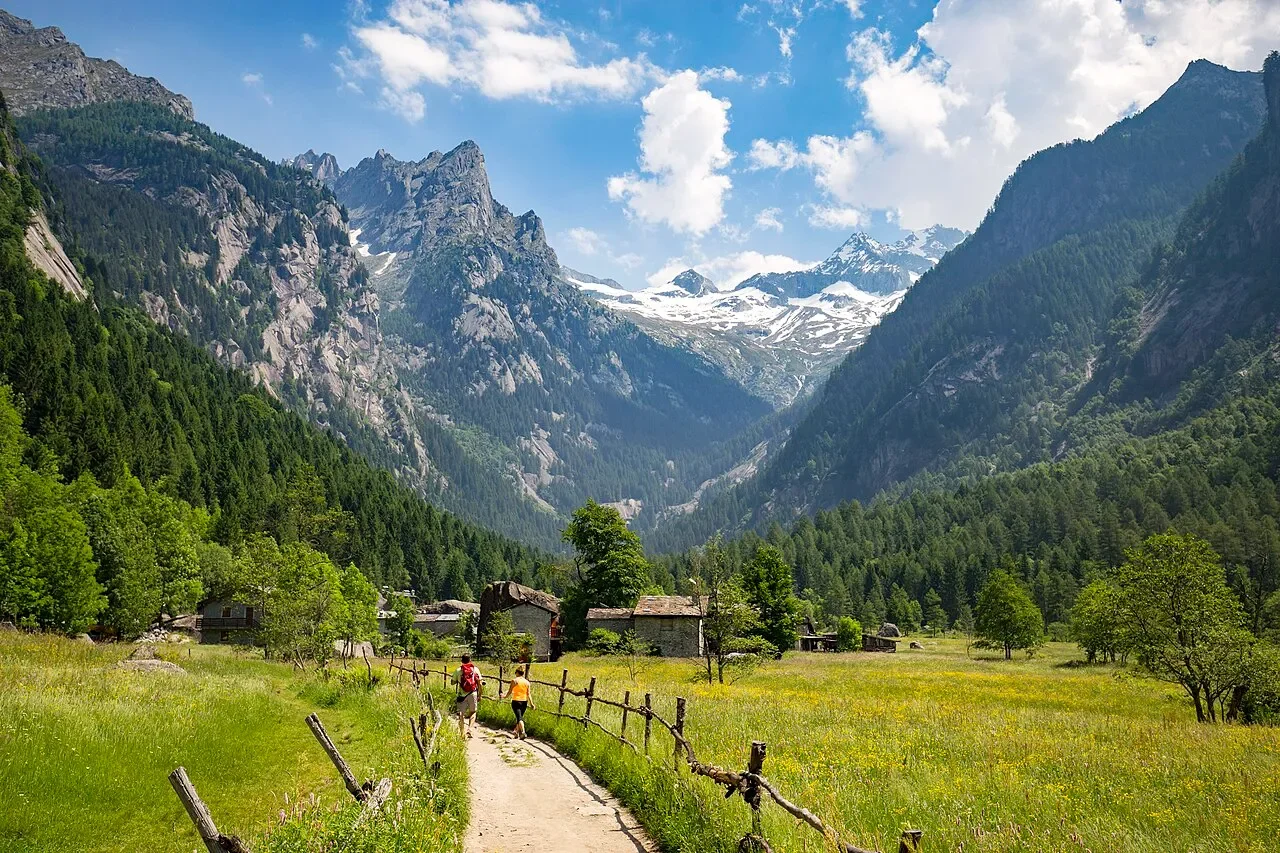 A footpath and stone huts among Val di Mello’s meadows, with high mountain peaks beyond.