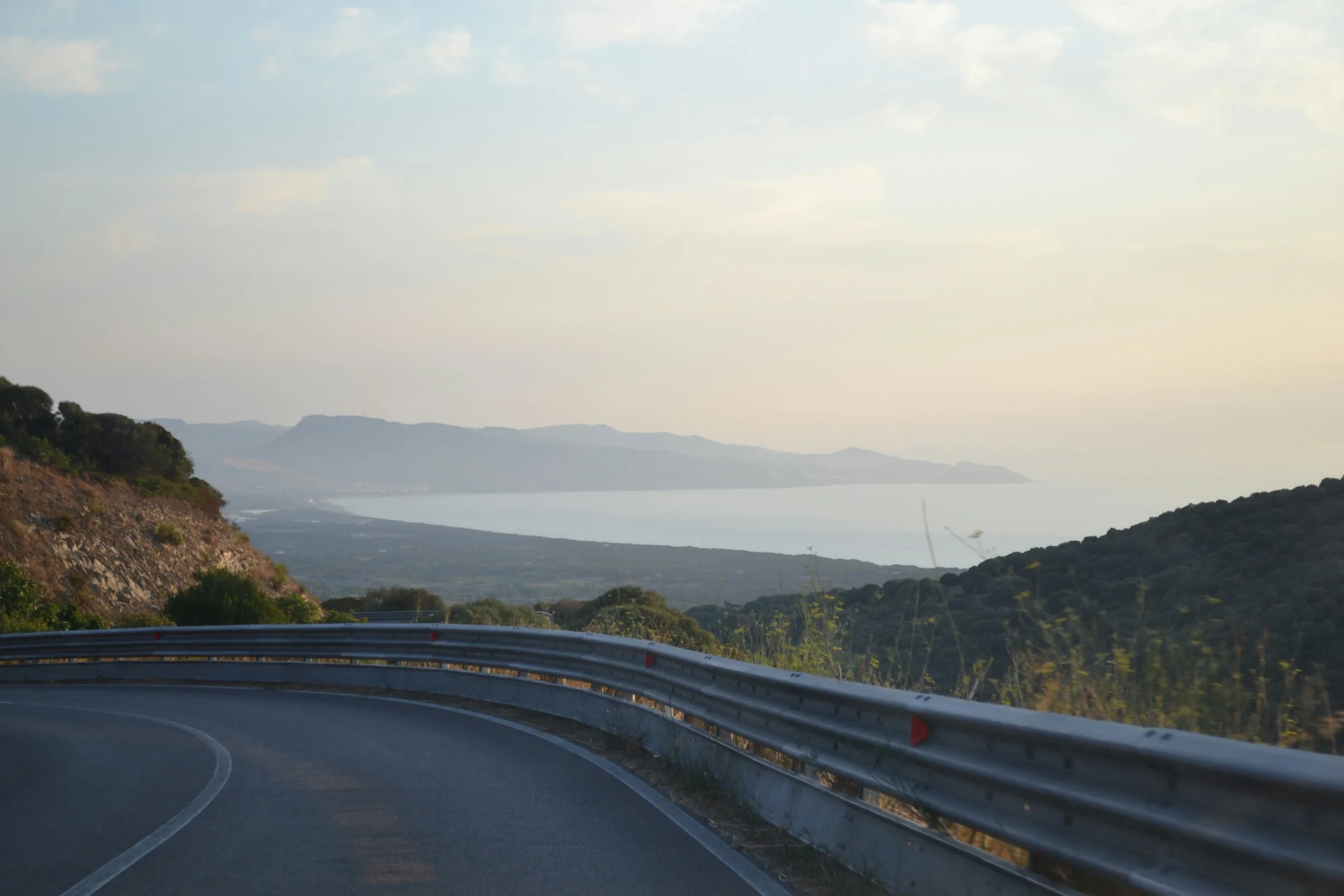 Scenic coastal road through the hills of Sardinia, overlooking the Mediterranean Sea and distant mountains