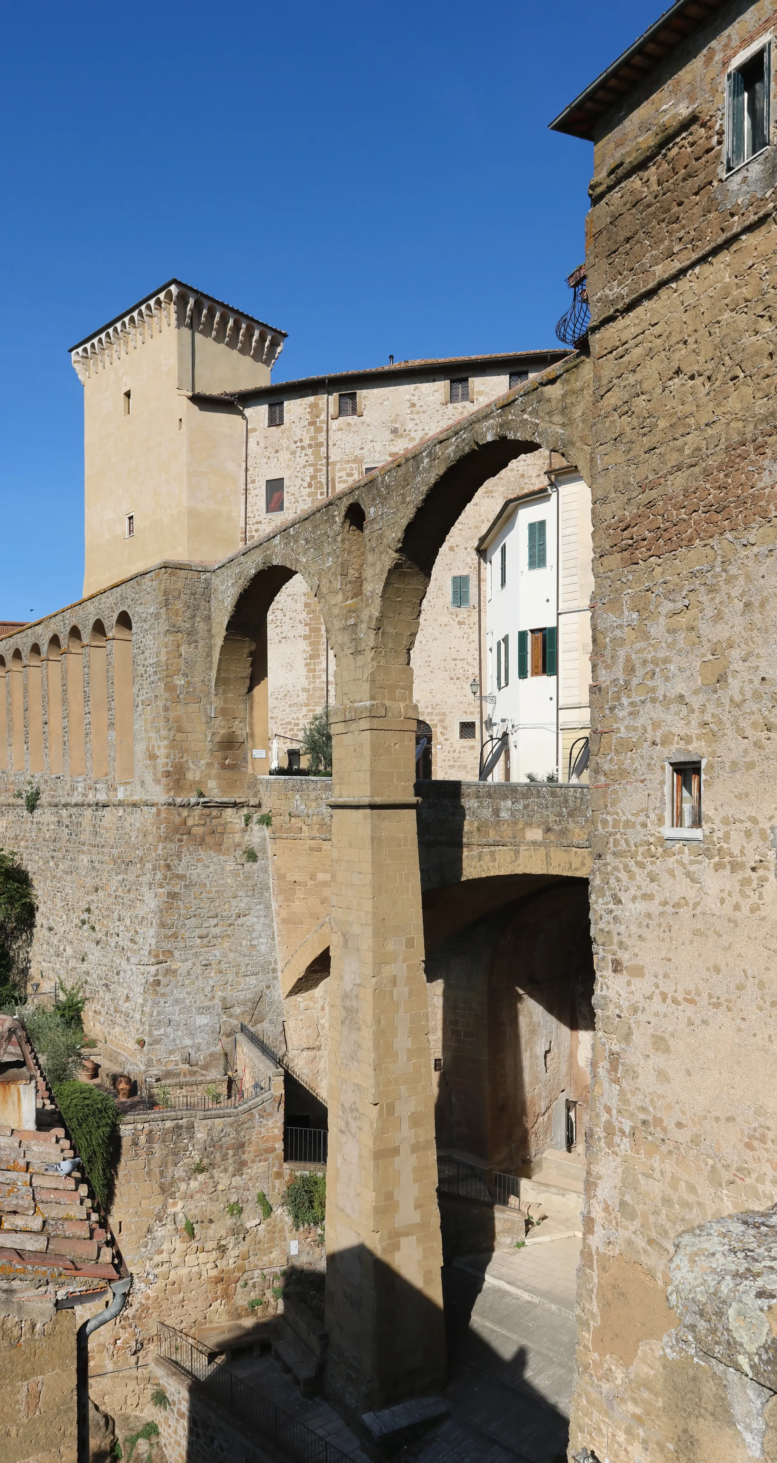 Tall stone arches of the Medici aqueduct beside historic buildings in Pitigliano.