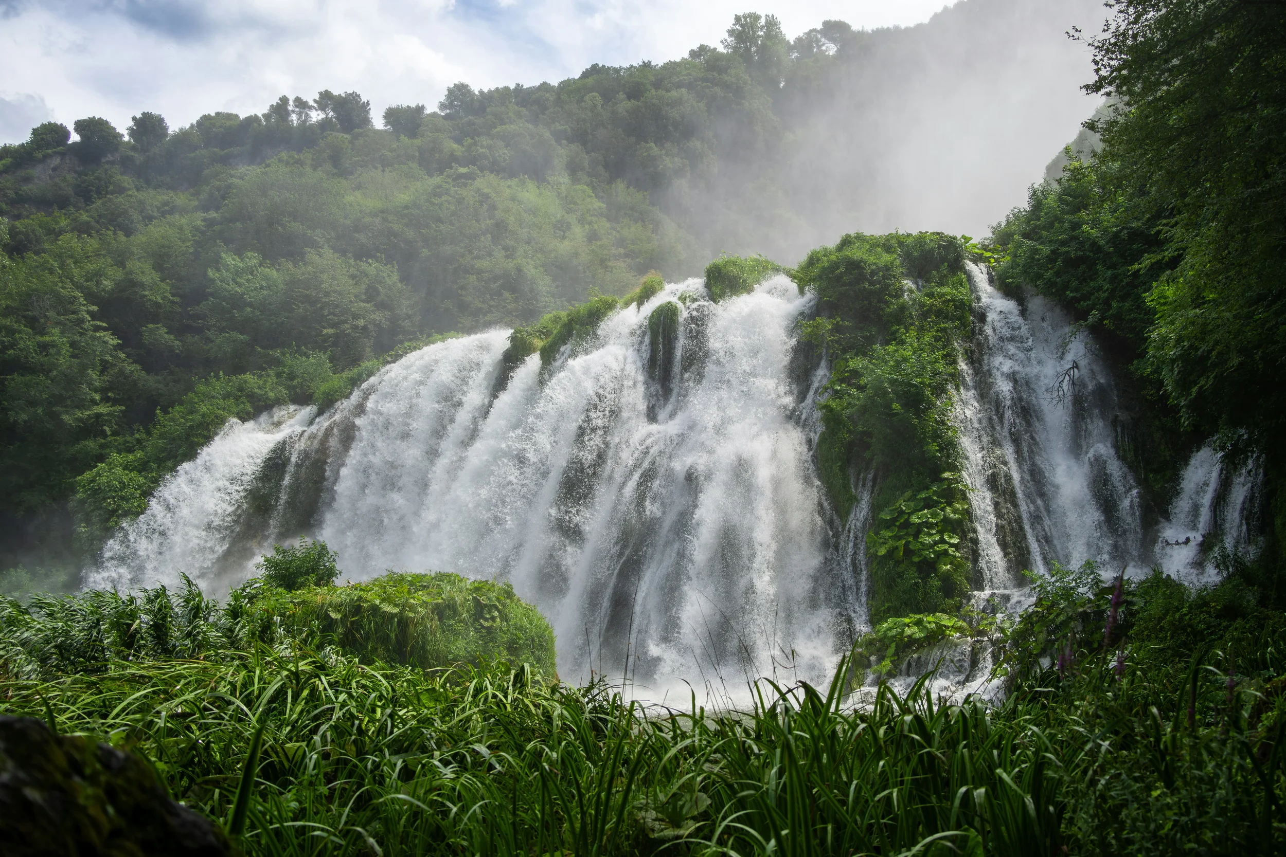 Cascata delle Marmore in Umbria, with white cascades tumbling over lush green rocks surrounded by dense woodland.