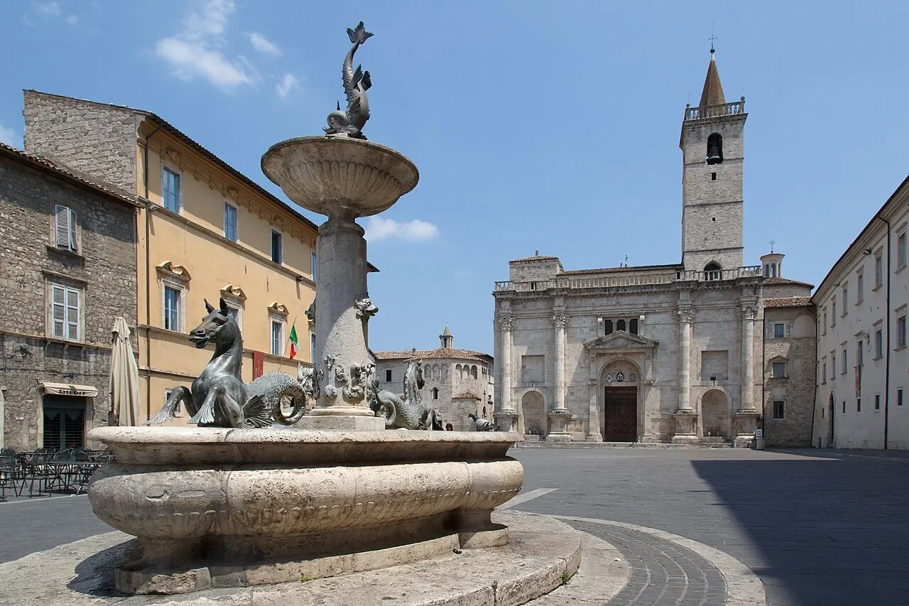 A sculpted fountain in Piazza Arringo, with the Cathedral of Sant’Emidio and its bell tower behind